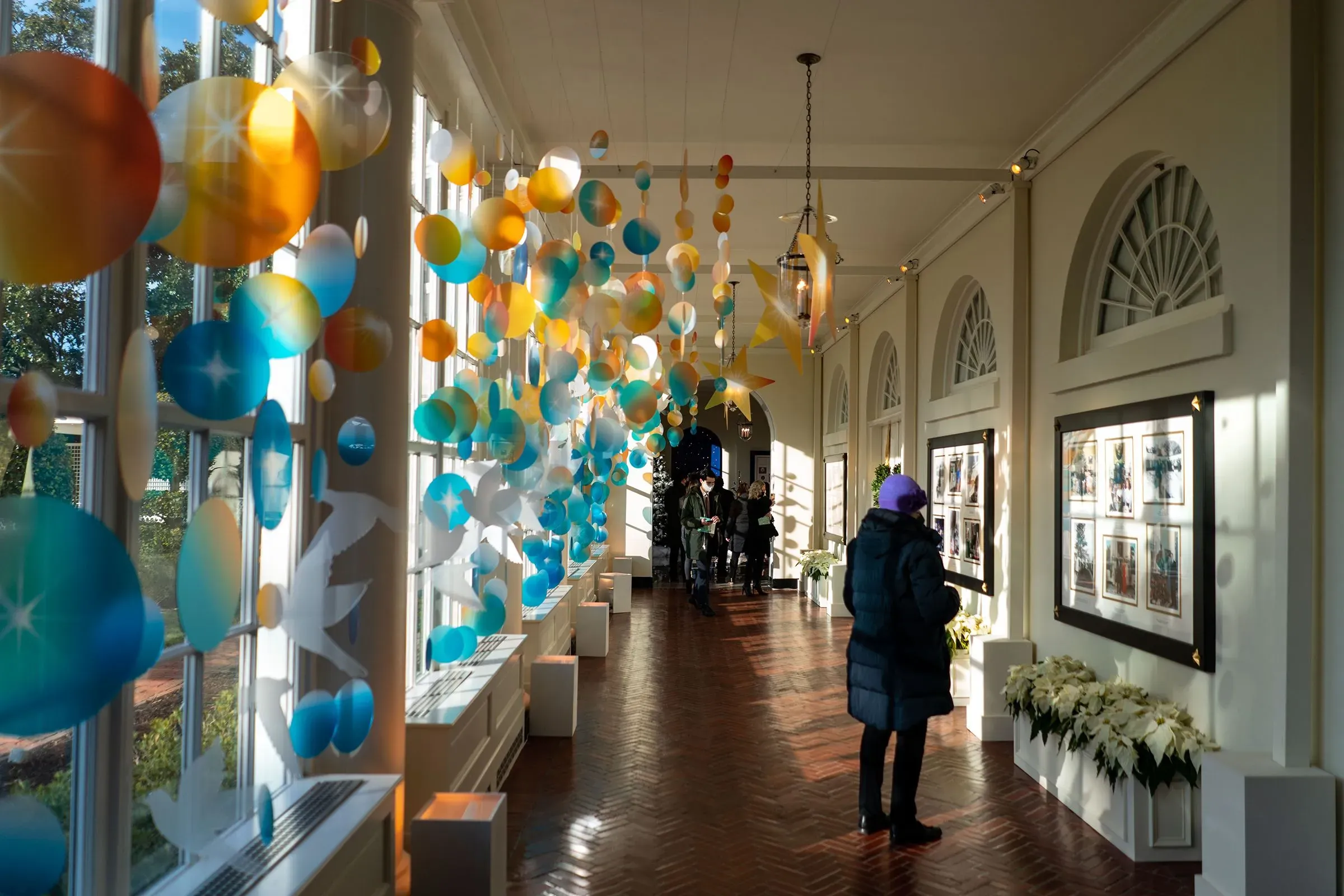 ممر مزين بكُرات ملونة وزهور، حيث يتجول الزوار في البيت الأبيض، مع صور مؤطرة على الجدران، تعكس تاريخ المكان.