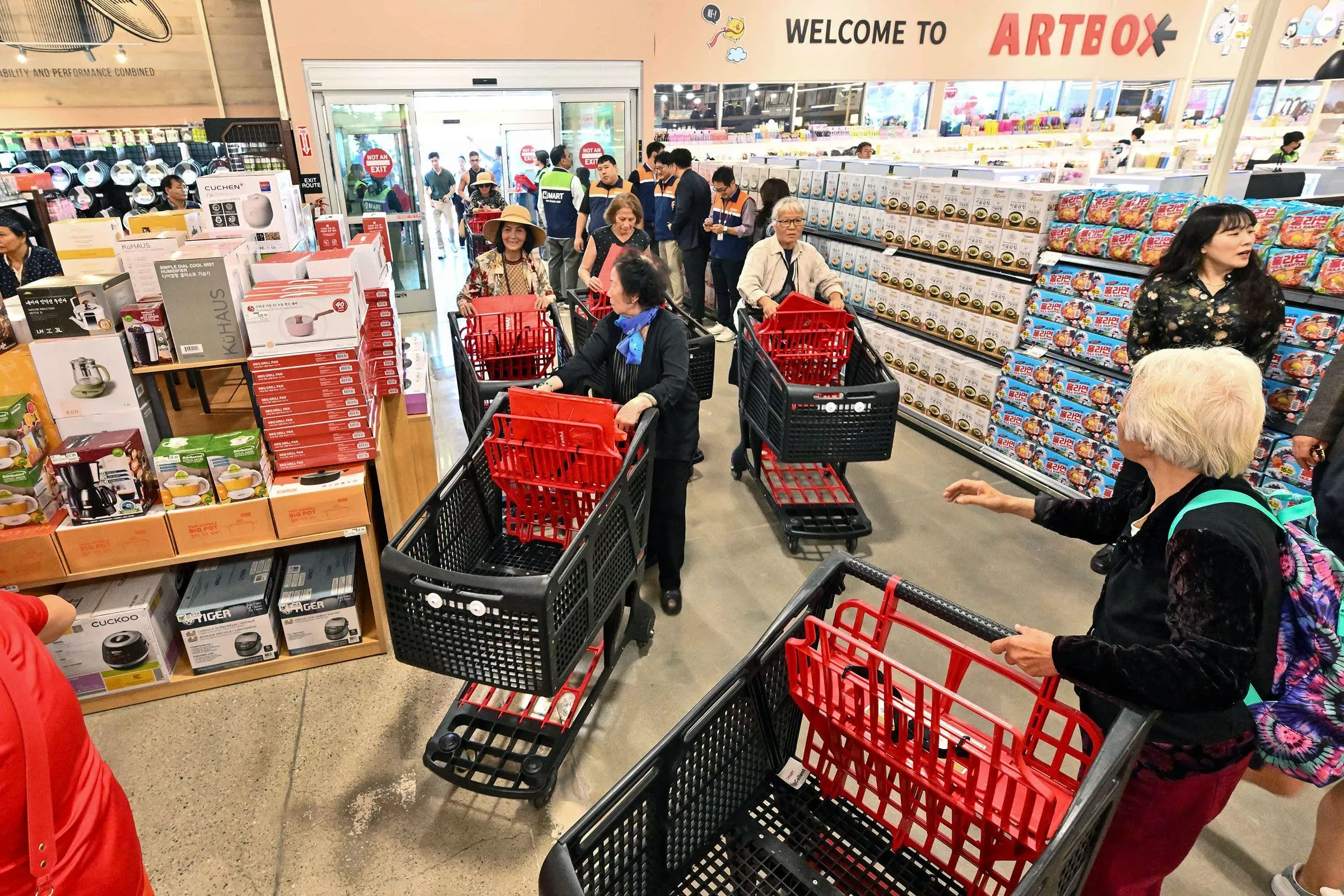 متسوقون في متجر حديث يحملون عربات تسوق، معروضات متنوعة من المنتجات في الخلفية، تعكس النشاط التجاري وسط تدهور سوق الوظائف.