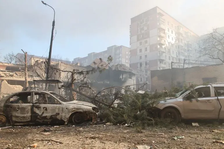 تظهر الصورة مشهدًا مدمرًا لمدينة أوكرانية بعد قصف، حيث تضررت السيارات والمباني، مما يبرز آثار الحرب المستمرة.