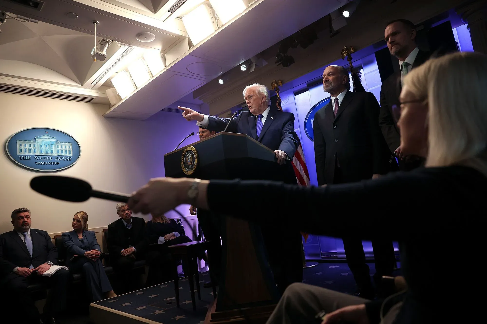 مؤتمر صحفي في البيت الأبيض حيث يتحدث مسؤول حكومي عن التعريفات الجمركية الجديدة، مع وجود الصحفيين في الخلفية.