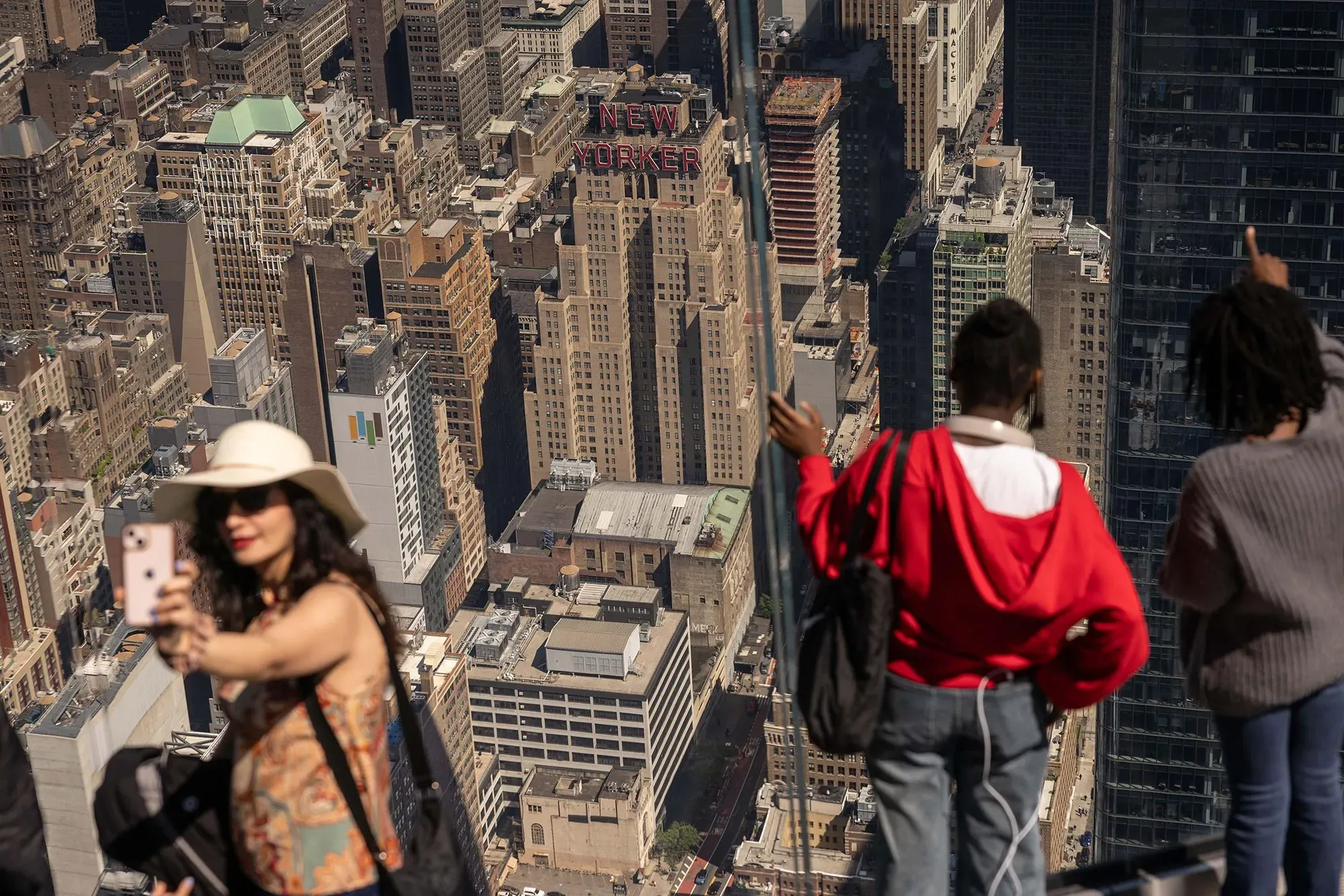 مجموعة من الأشخاص يستمتعون بإطلالة على مدينة نيويورك، حيث تظهر المباني الشاهقة وعلامة "NEW YORKER" في الخلفية.