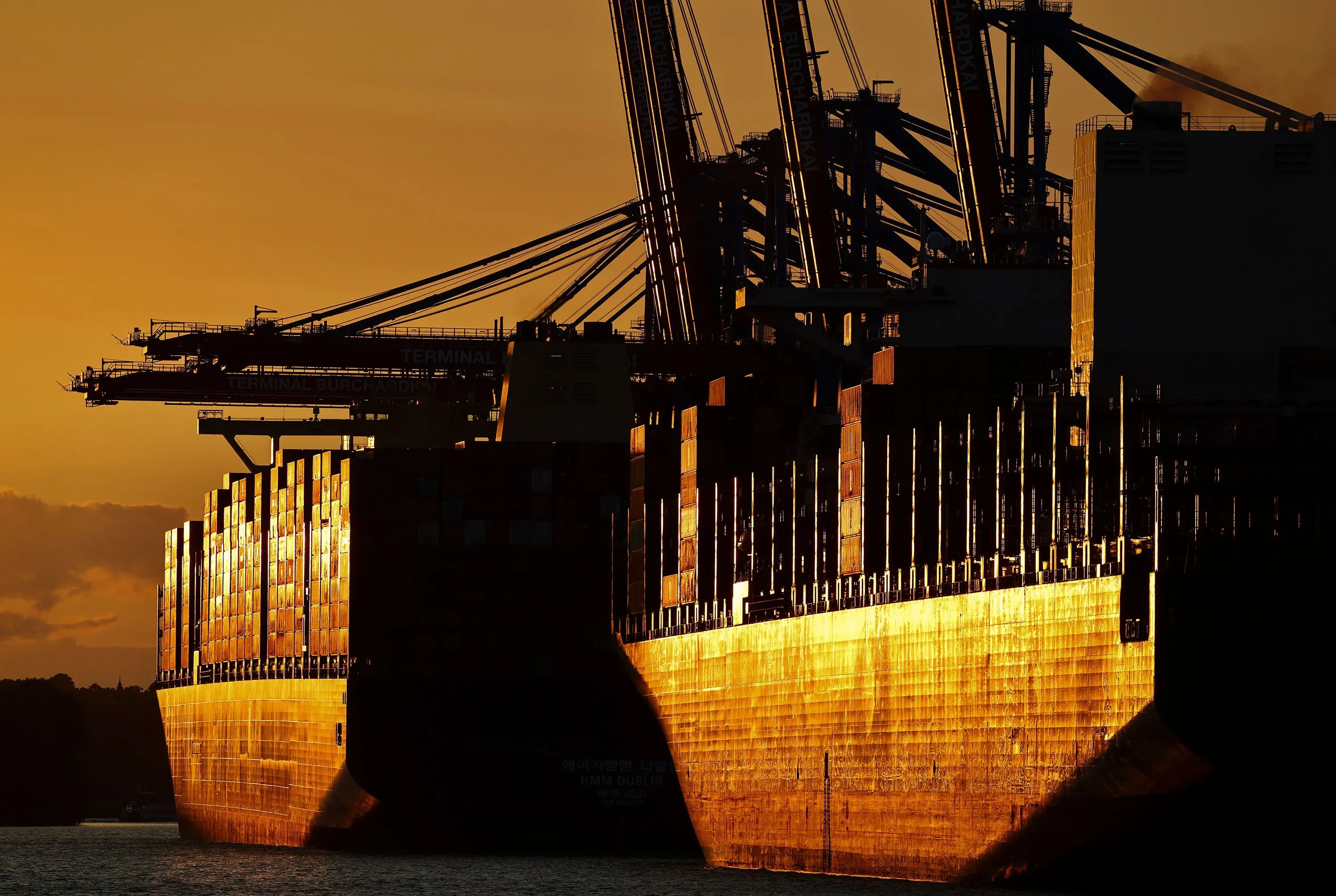 صورة لميناء شحن عند غروب الشمس، حيث تظهر السفن الكبيرة والأجهزة اللوجستية، مما يعكس أهمية الإحصاءات الاقتصادية في التجارة.