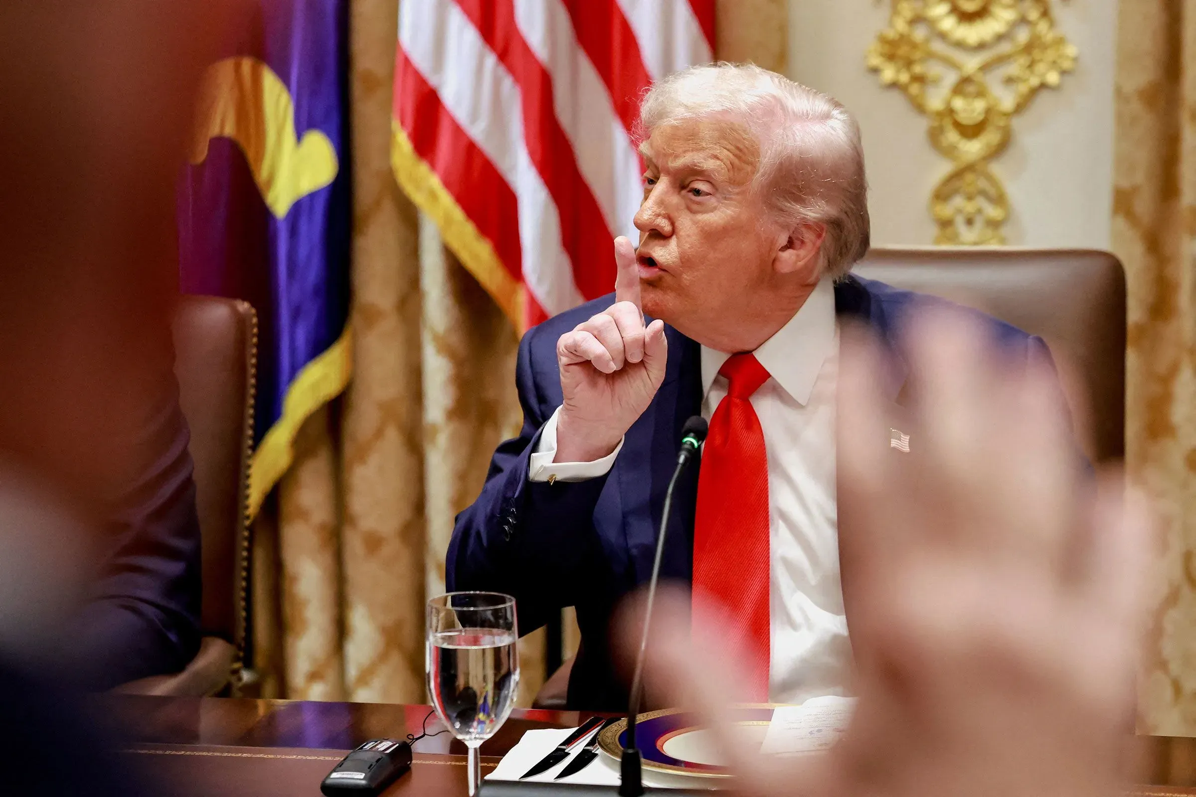 ترامب يتحدث خلال اجتماع في البيت الأبيض، مع العلم الأمريكي في الخلفية، مع التركيز على قضايا الإنفاق الحكومي وتأثير الإغلاق.