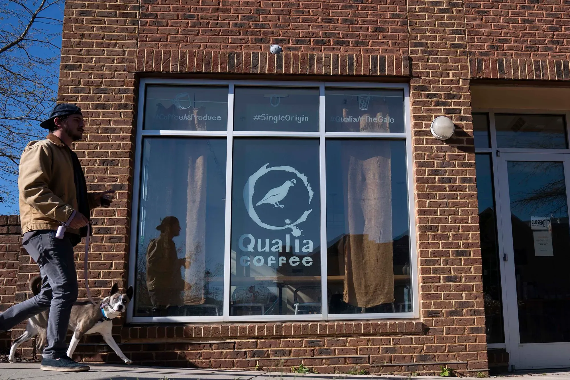 شخص يسير مع كلبه أمام واجهة متجر "Qualia Coffee" في واشنطن، حيث تتأثر أسعار القهوة بارتفاع الرسوم الجمركية.