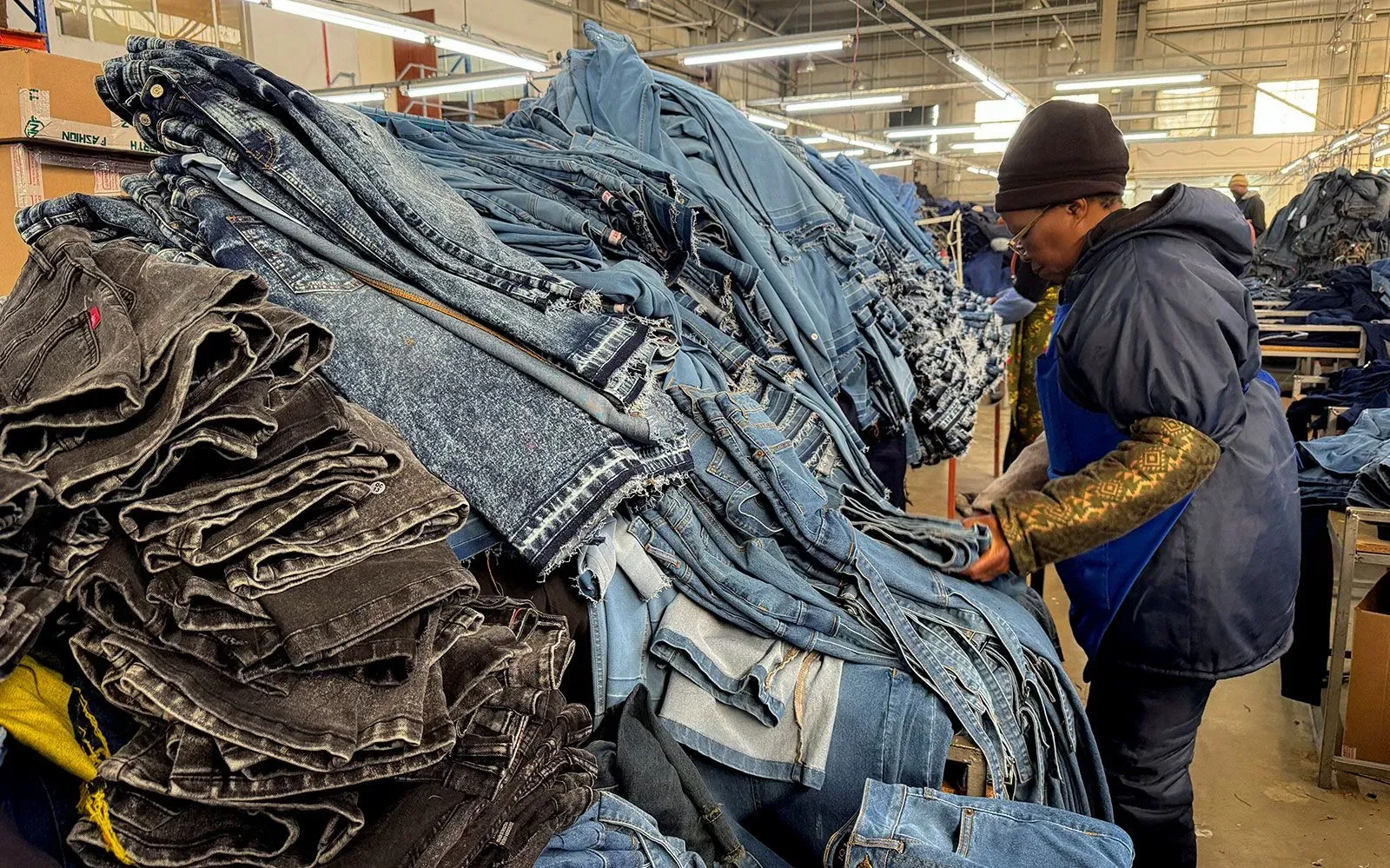عامل يعمل في مصنع للملابس يقوم بترتيب أكوام من السراويل الجينز، مما يعكس تأثير التعريفات الجمركية الأمريكية على صناعة النسيج في أفريقيا.