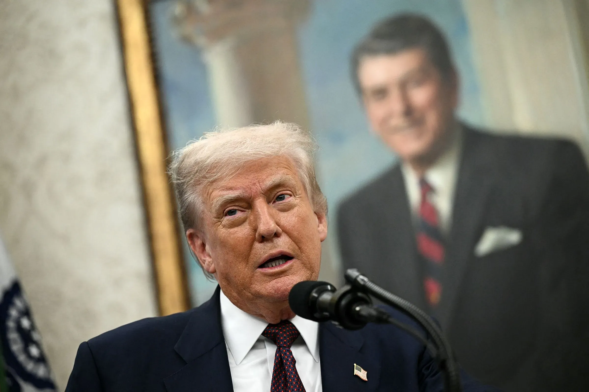 ترامب يتحدث أمام ميكروفون في المكتب البيضاوي، مع صورة للرئيس الأسبق رونالد ريغان خلفه، يعبر عن استعداده لاستخدام الجيش في إنفاذ القانون.