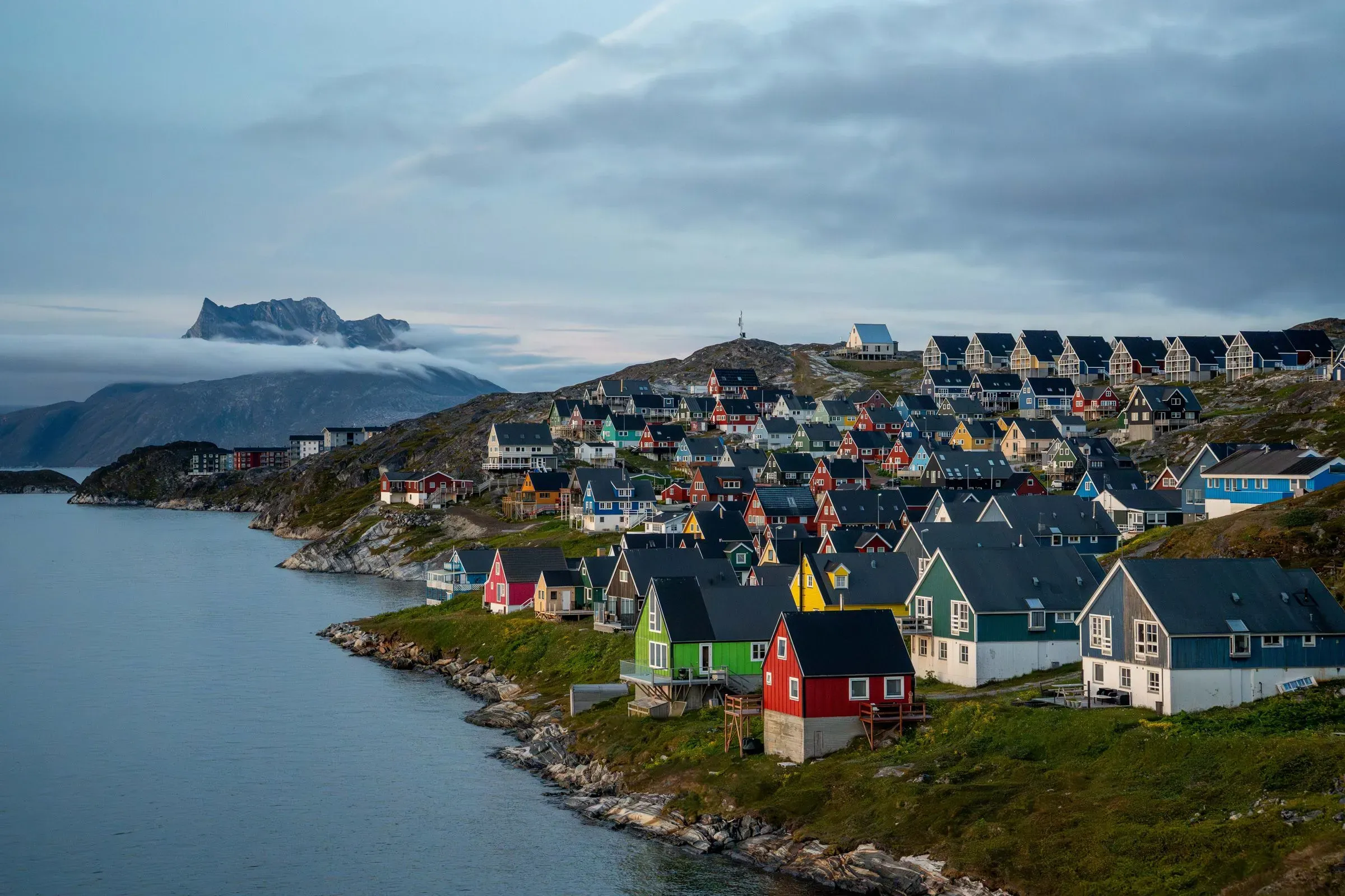 منظر لقرية في غرينلاند، تظهر منازل ملونة محاطة بالطبيعة الخلابة، مما يعكس الحياة اليومية في هذه المنطقة القطبية.