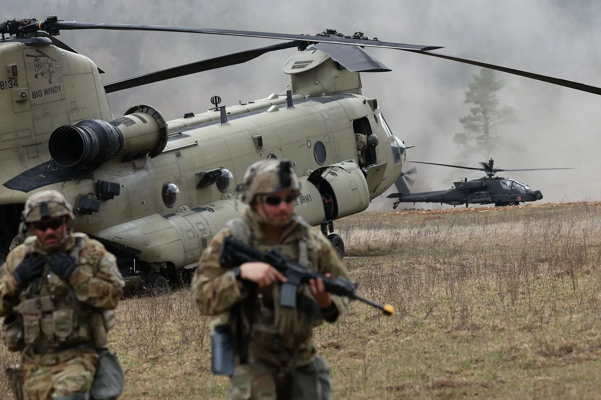 جنود أمريكيون يرتدون زيهم العسكري أثناء مناورات عسكرية، مع مروحية عسكرية في الخلفية، تعكس التوترات الجيوسياسية الحالية.