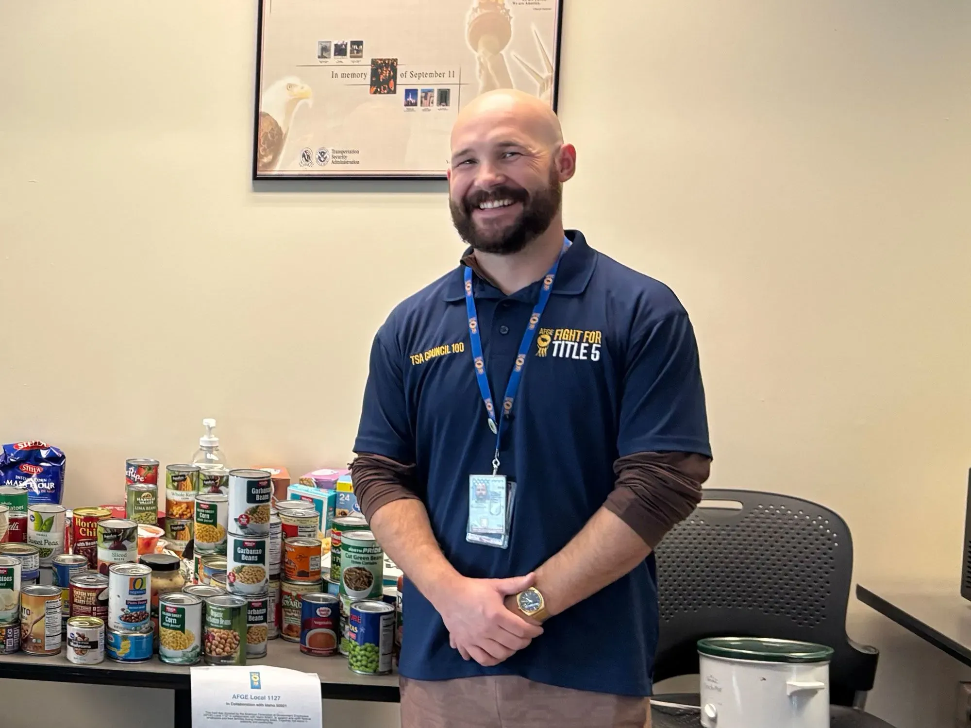 موظف في إدارة أمن النقل يقف مبتسمًا أمام طاولة مليئة بعلب الطعام، يعكس جهود الدعم للموظفين خلال فترة الإغلاق الحكومي.