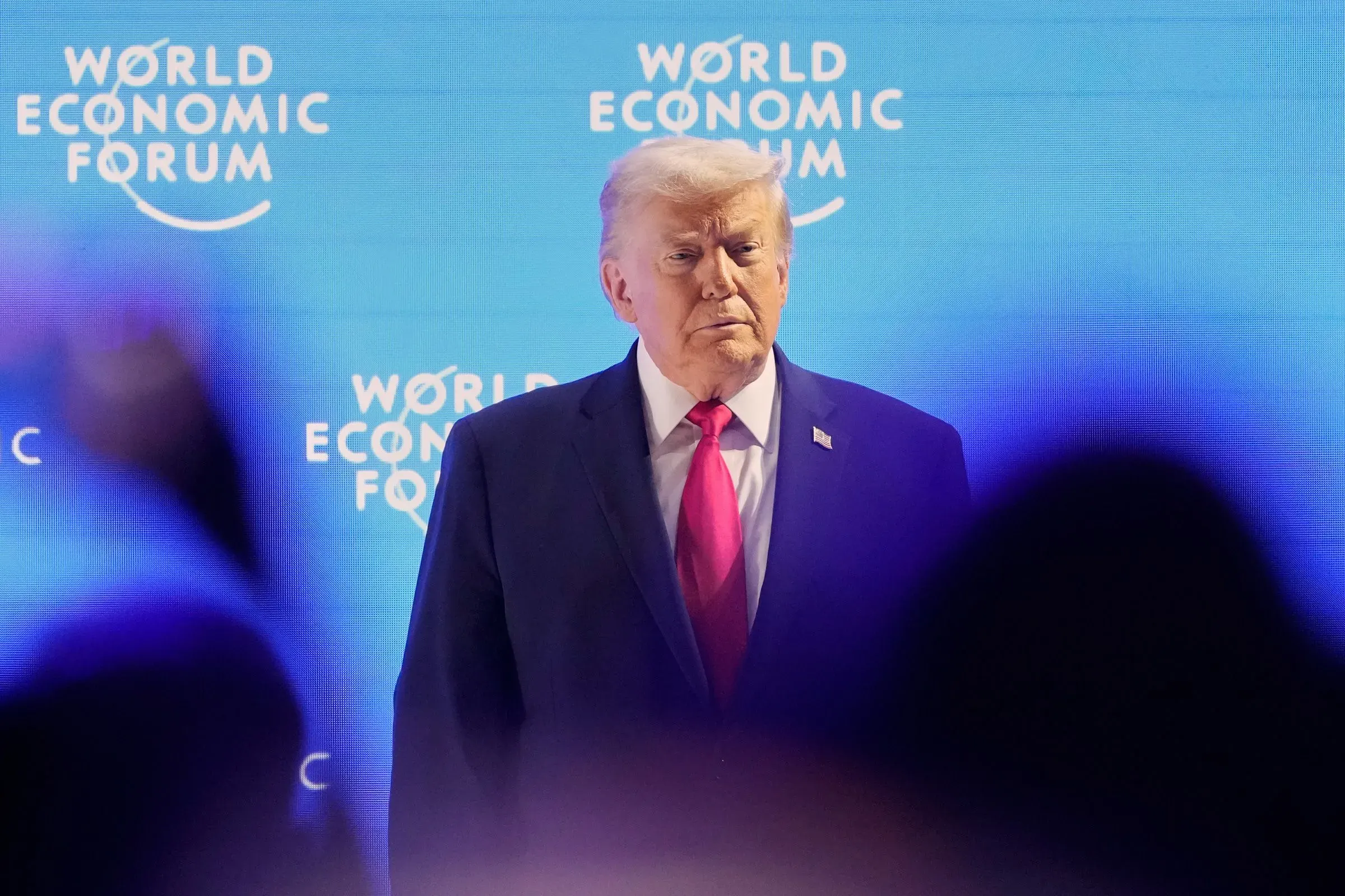 ترامب يظهر في منتدى الاقتصاد العالمي، مع خلفية تحمل شعار المنتدى، مع تعبير وجه يعكس الجدية وسط أجواء متوترة.