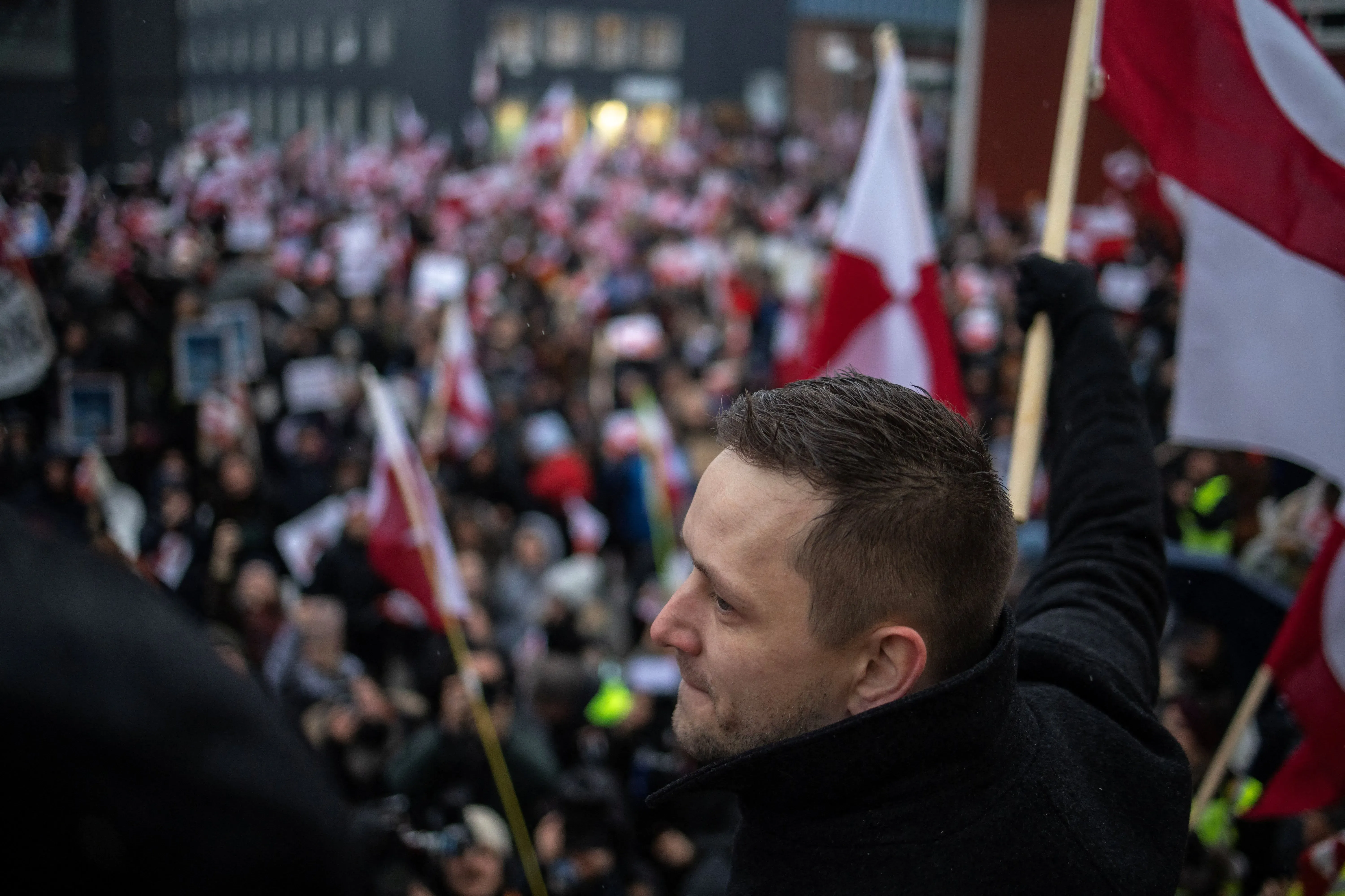 محتجون يحملون لافتات وأعلام في تجمع حاشد، مع التركيز على أحد المتظاهرين في المقدمة، في سياق الغضب الشعبي ضد سياسات ترامب.