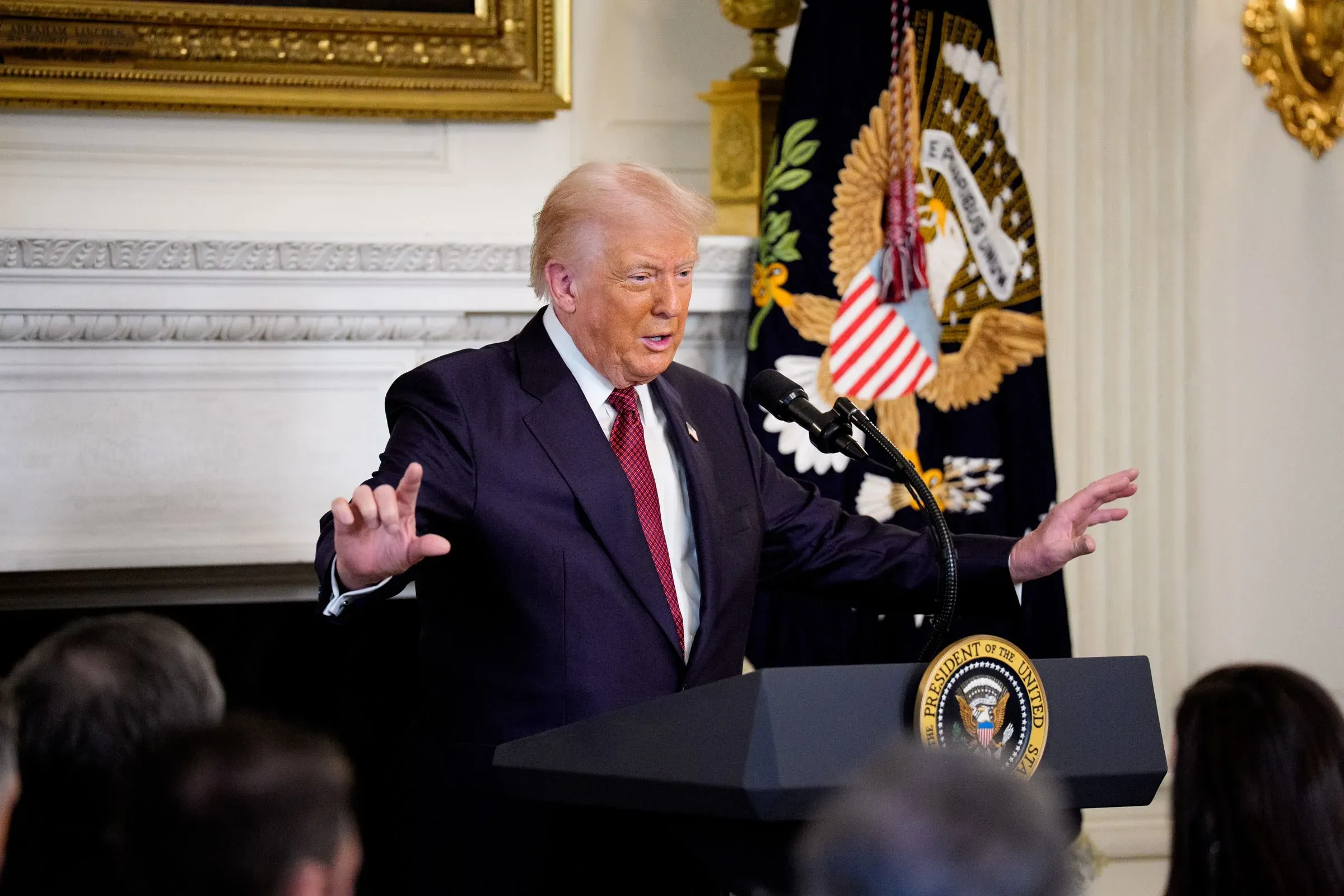 دونالد ترامب يتحدث خلال مؤتمر صحفي، مع وجود العلم الأمريكي وشعار الرئاسة خلفه، معبرًا عن سلطته وسط تحديات سياسية.