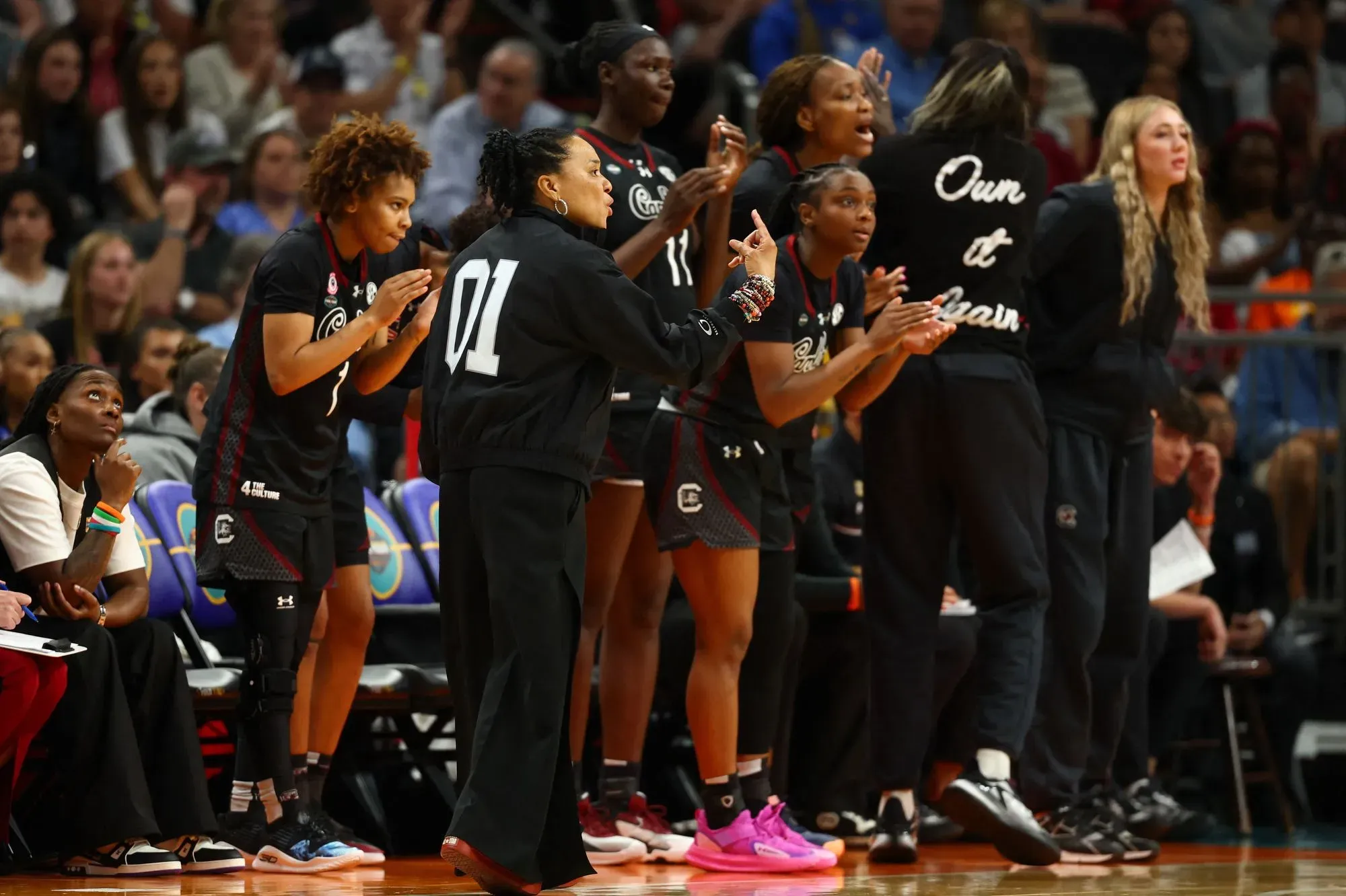 فريق كارولينا الجنوبية يشجع بنشاط خلال مباراة البطولة، مع تعبيرات حماسية من المدرب واللاعبات في الخلفية.