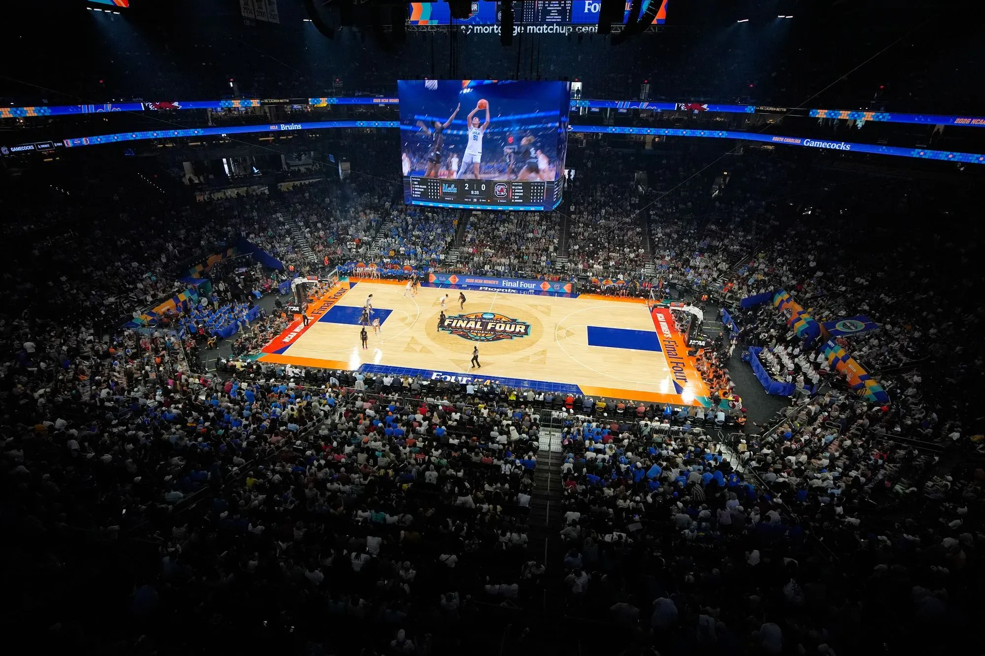 مدرج مزدحم خلال مباراة نهائي كرة السلة للسيدات بين جامعة كاليفورنيا في لوس أنجلوس وكارولينا الجنوبية، مع عرض النتائج على الشاشة الكبيرة.