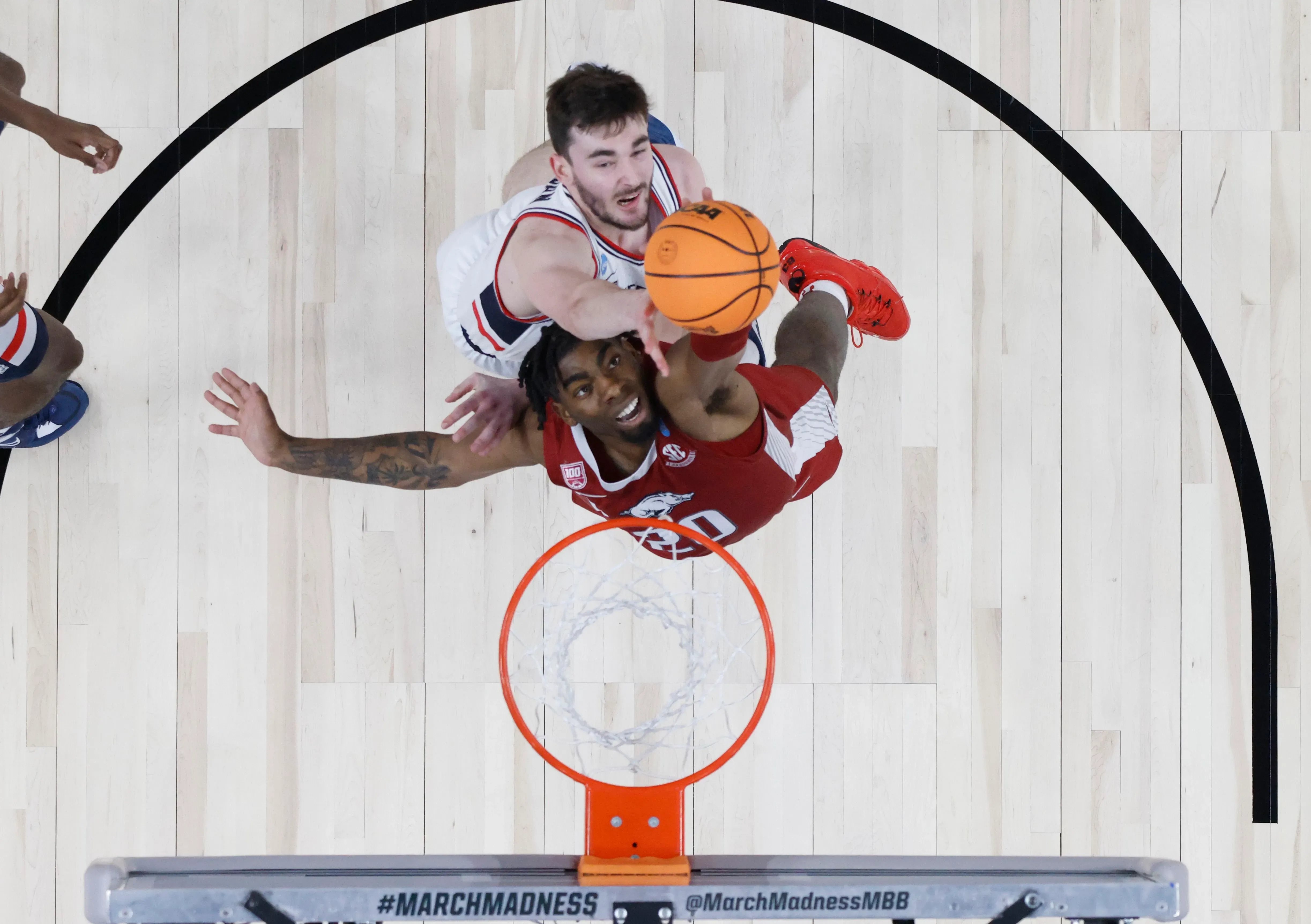 لاعب كرة سلة يتنافس على الكرة في مباراة، مع التركيز على حركة القفز نحو السلة. تظهر تفاصيل الساحة واللاعبين الآخرين في الخلفية.