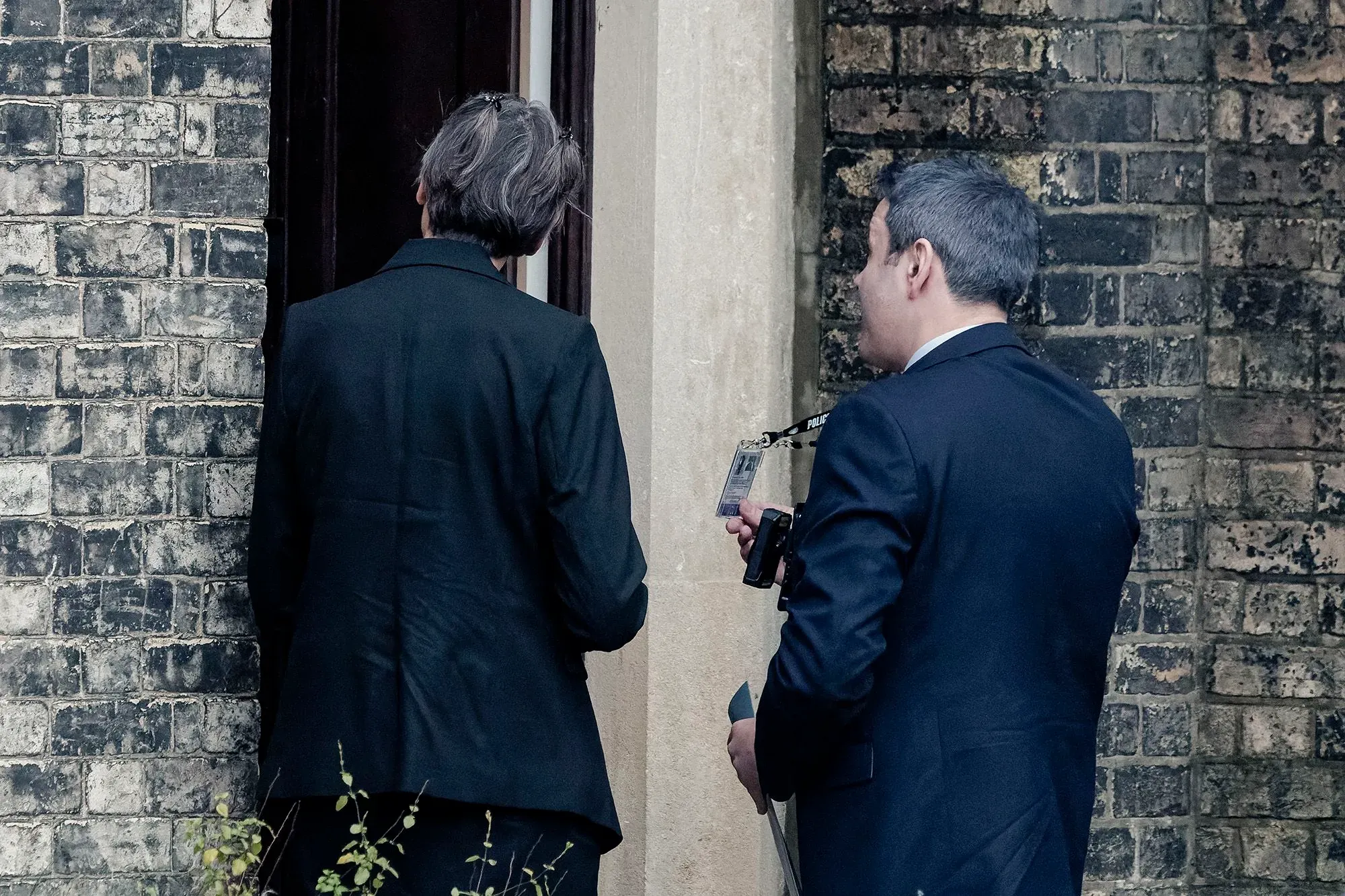 عميلان من الشرطة البريطانية يقفان أمام باب منزل، أحدهما يحمل بطاقة تعريف، في إطار تحقيق بشأن سوء السلوك في المناصب العامة.
