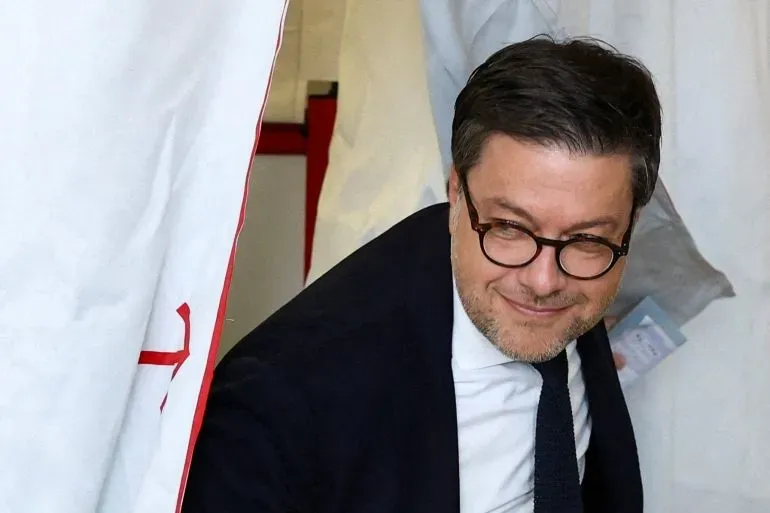 رجل يرتدي نظارات ويبتسم وهو يخرج من صندوق الاقتراع في فرنسا، حيث تجرى الانتخابات المحلية لاختيار رؤساء البلديات.