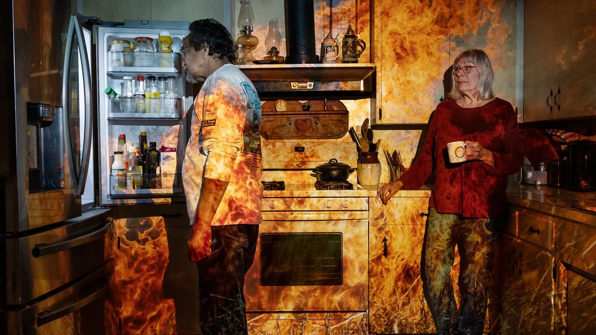 رجل يتفحص ثلاجته بينما تشتعل النيران في مطبخه، مما يبرز تأثير حرائق الغابات المتزايدة بسبب تغير المناخ.