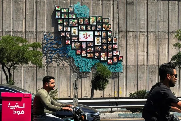 جدارية ملونة في طهران تضم صورًا لأشخاص، تعكس الثقافة الإيرانية، بينما يمر سائقو دراجات نارية بجوارها.