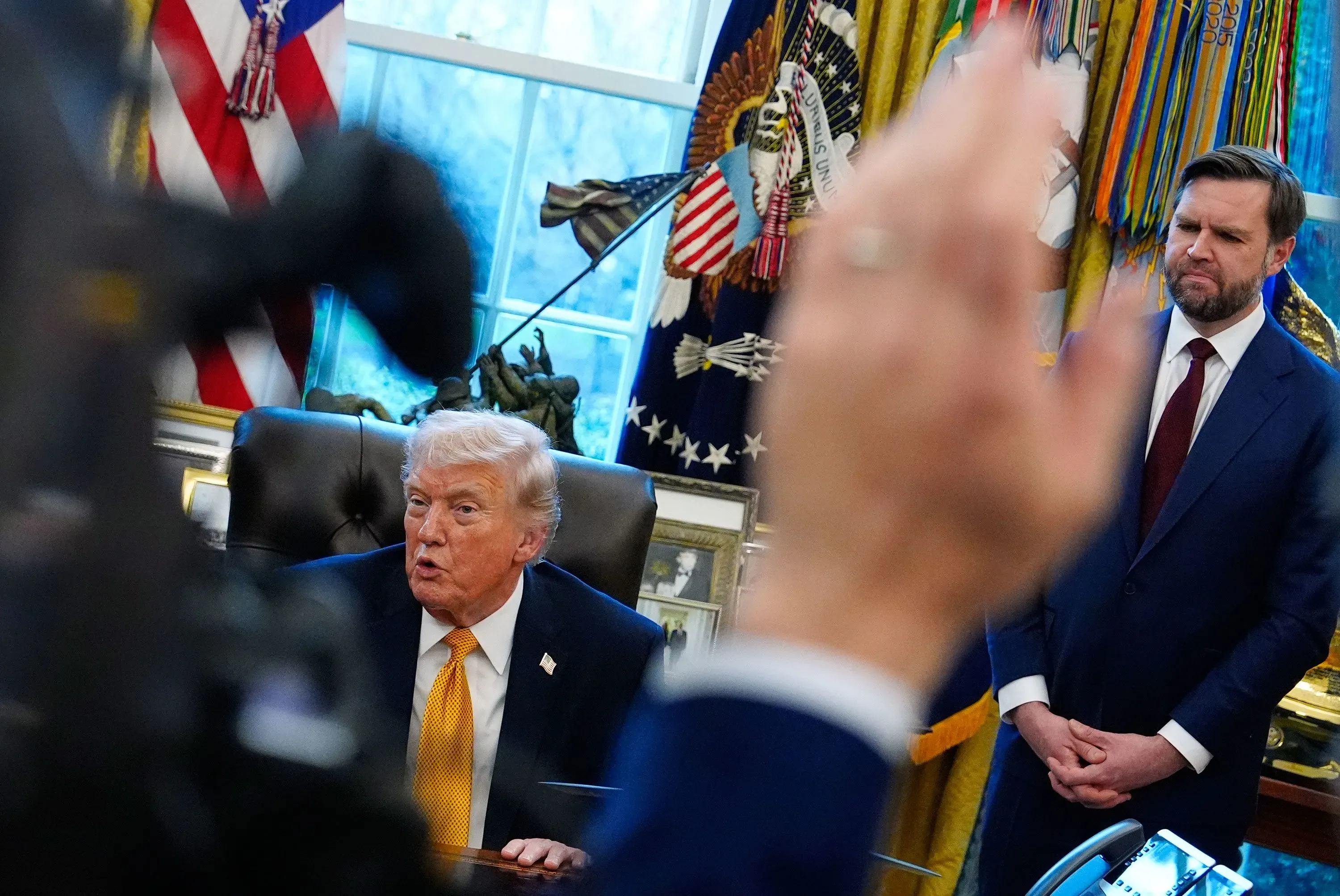 اجتماع في المكتب البيضاوي حيث يتحدث ترامب بينما يقف جيه دي فانس بجانبه، مع أعلام خلفية تعكس الأجواء السياسية المتوترة.