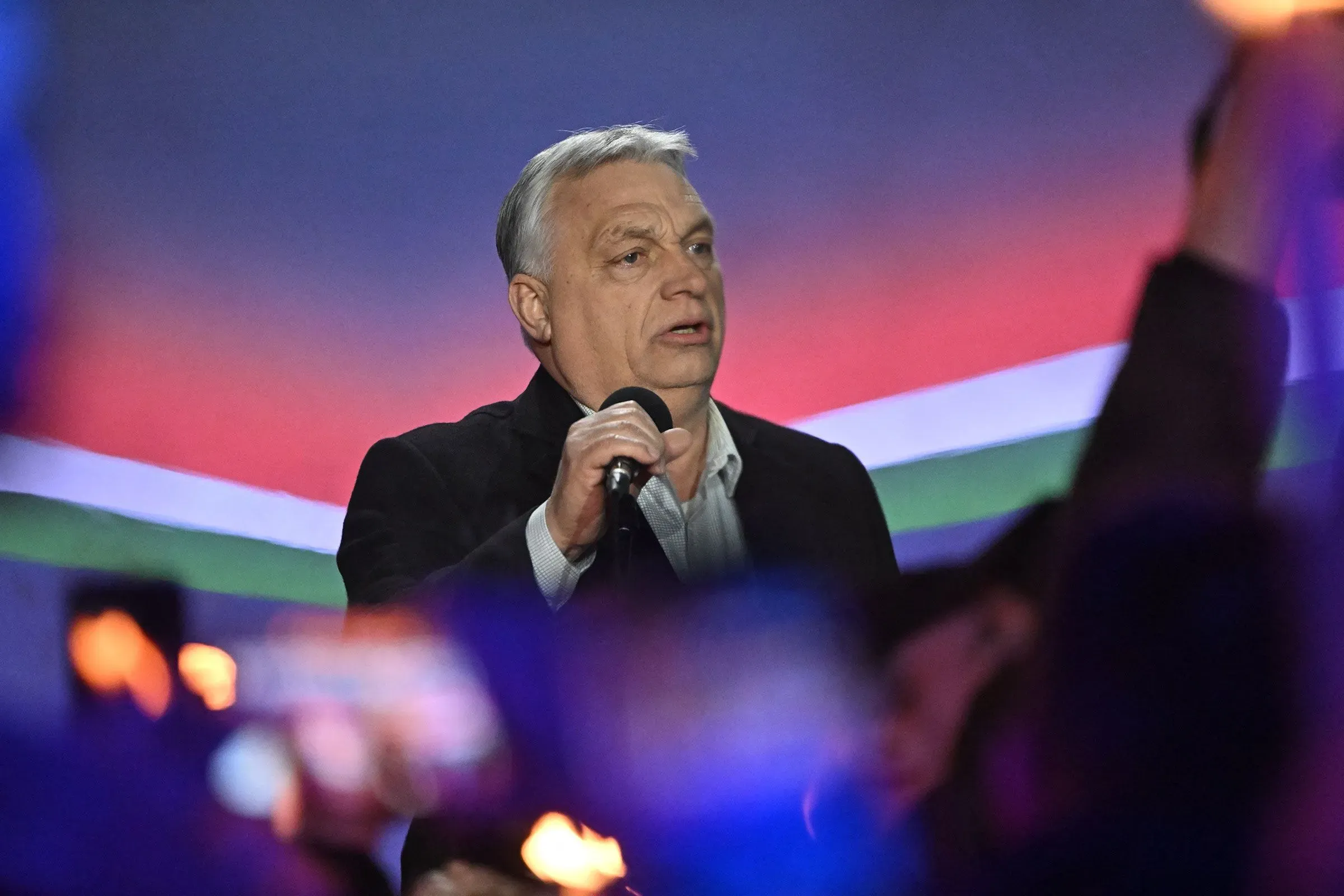 رئيس الوزراء المجري فيكتور أوربان يتحدث في تجمع حاشد، مع خلفية ملونة تعكس العلم المجري، وسط تفاعل الجمهور.