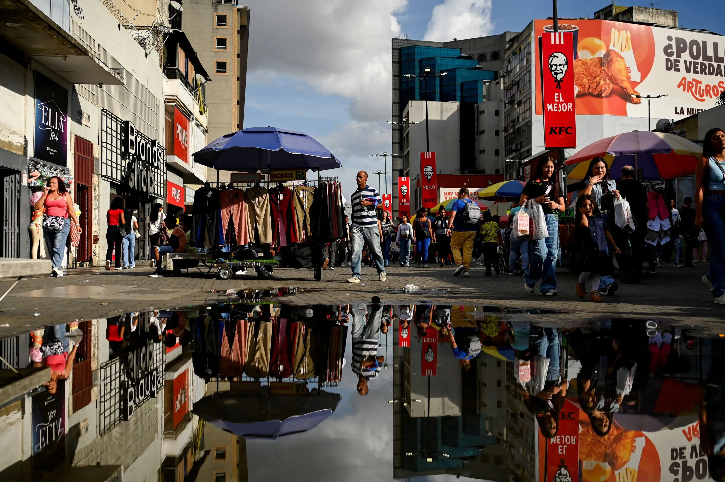 مشهد مزدحم في مركز تسوق بكراكاس، حيث يتجول المتسوقون بين المحلات، مع وجود طابور أمام متجر للملابس الداخلية بسبب التخفيضات.