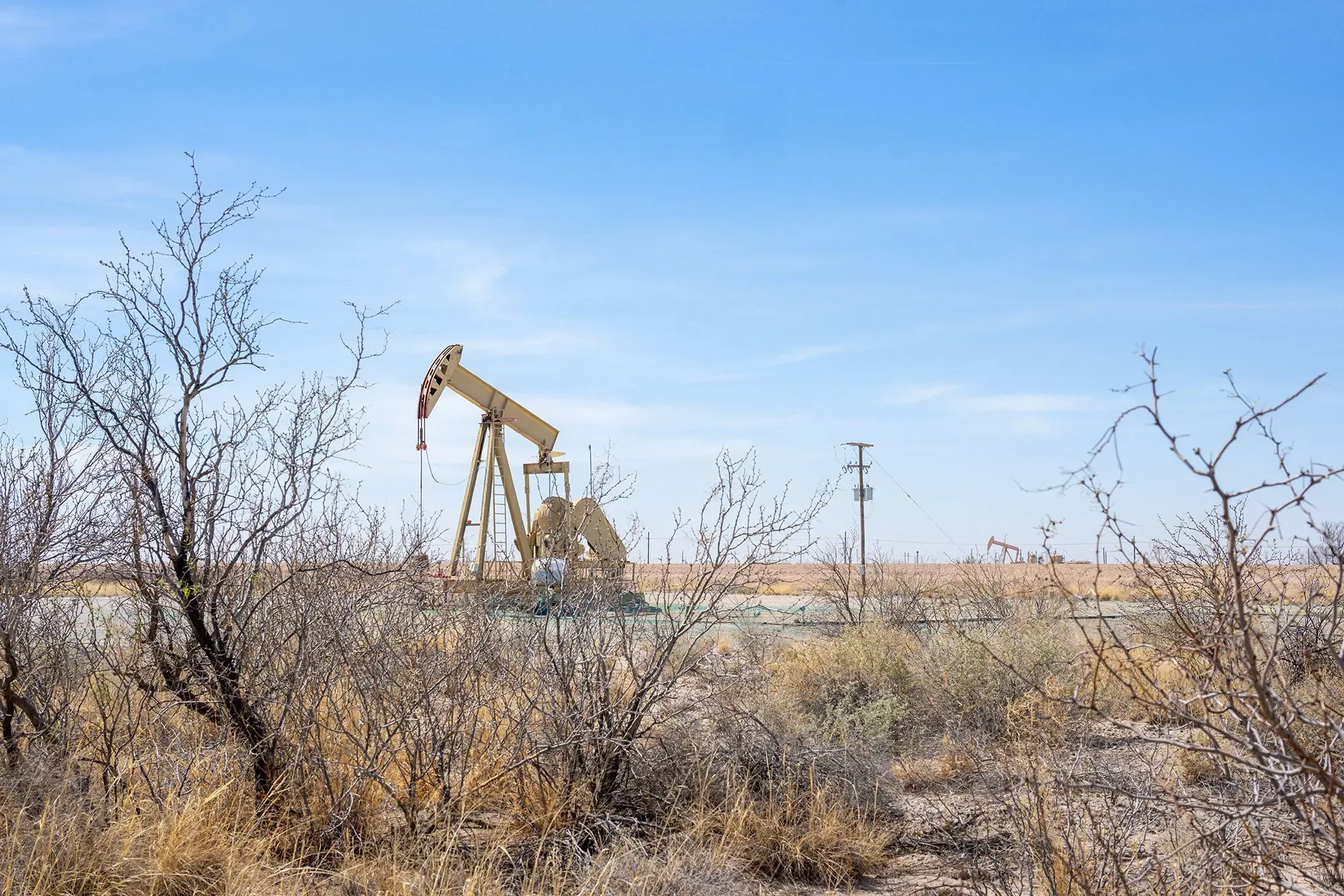 مضخة نفط تعمل في منطقة جافة، محاطة بأشجار وشجيرات، تعكس تأثيرات إغلاق مضيق هرمز على سوق الطاقة العالمي.