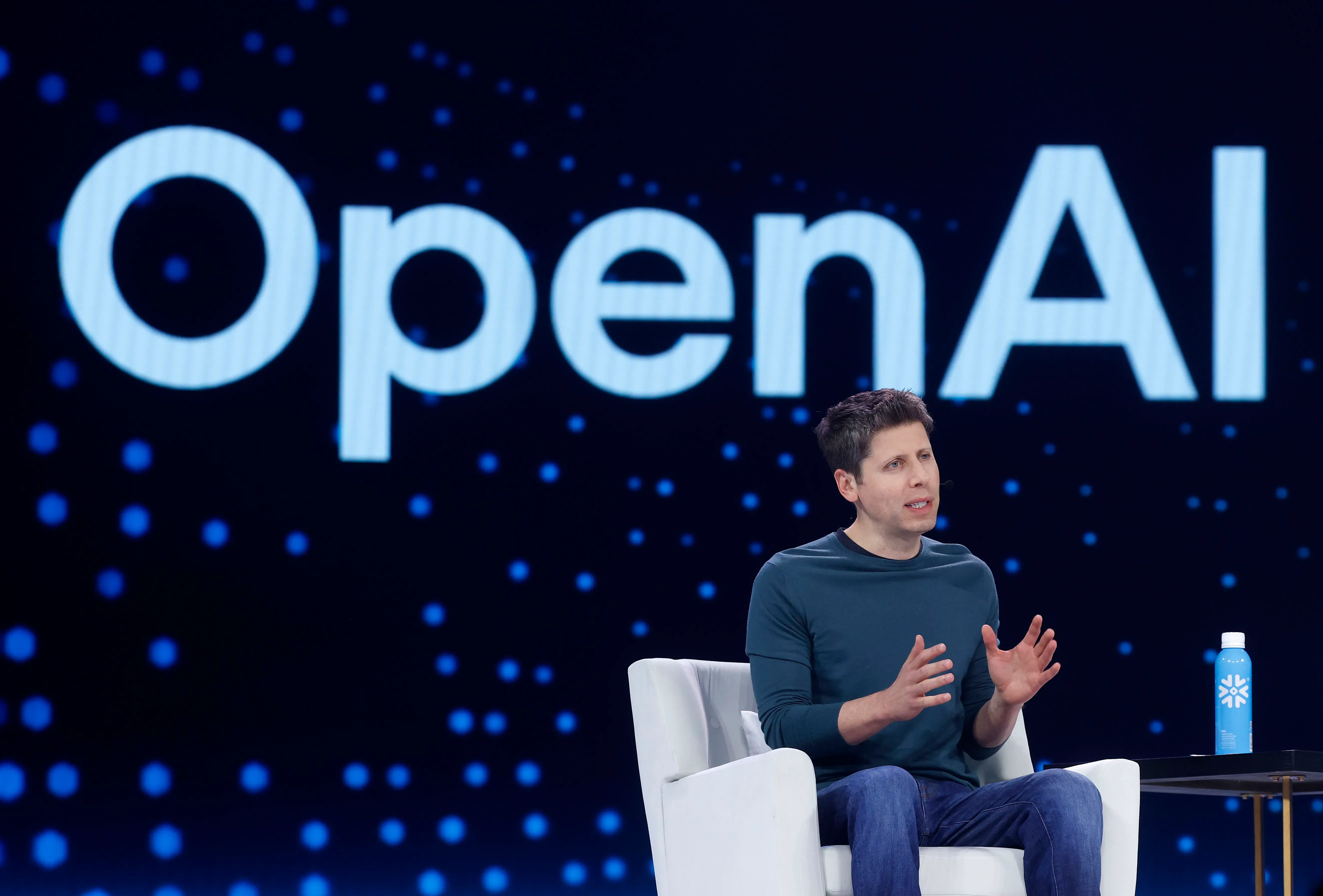 رجل يتحدث على منصة أمام شعار OpenAI، مع خلفية مضيئة، يعكس أهمية الشراكة بين OpenAI وNvidia في مجال الذكاء الاصطناعي.