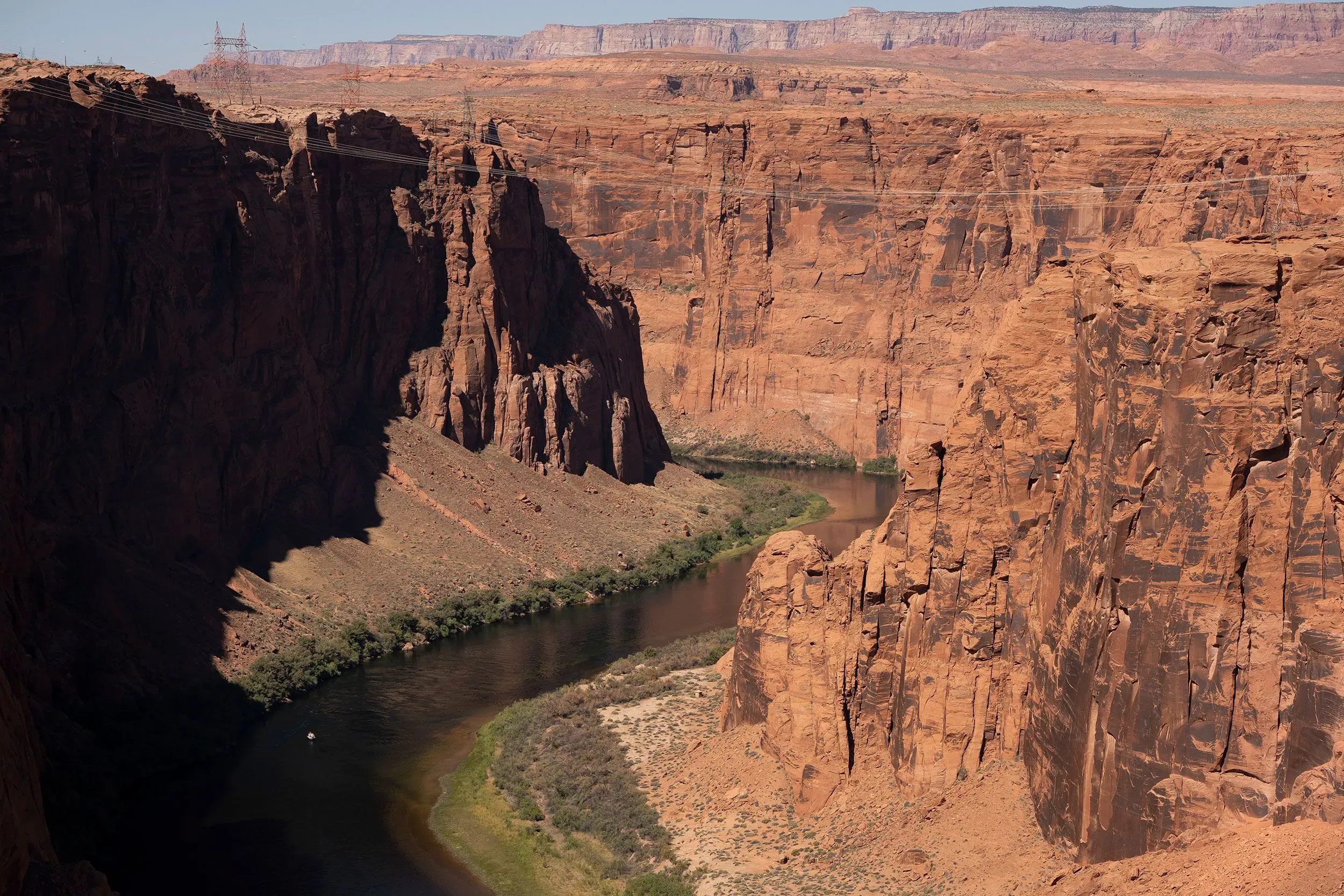 منظر لنهر كولورادو وهو يتدفق بين جدران صخرية حمراء، محاط بنباتات خضراء، مما يبرز أهمية النهر في دعم الحياة والاقتصاد في الغرب الأمريكي.