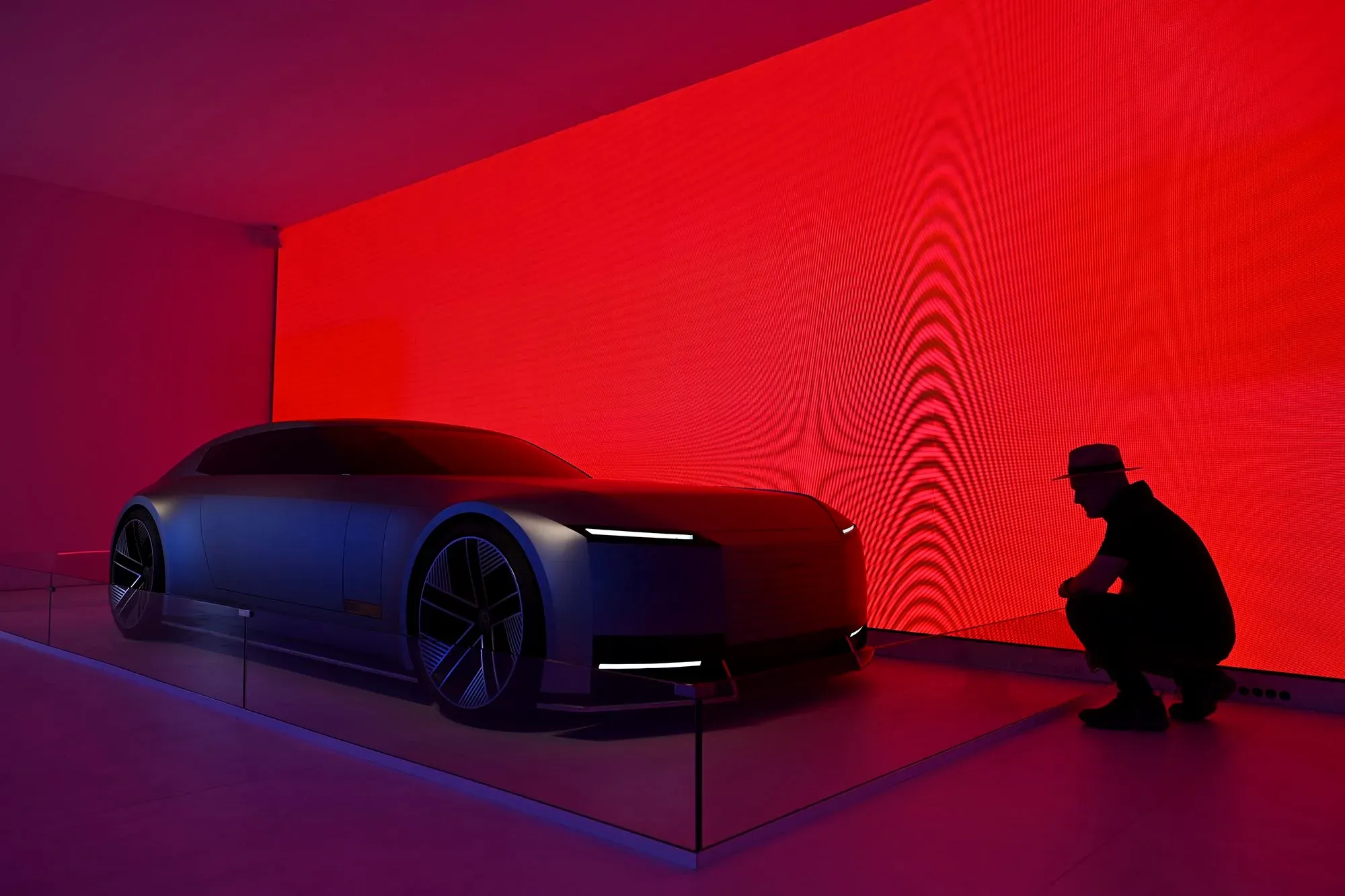 تصميم سيارة جاكوار التجريبية Type 00 مع خلفية حمراء زاهية، حيث يتفاعل شخص مع النموذج، مما يعكس توجه الشركة نحو الابتكار الكهربائي.