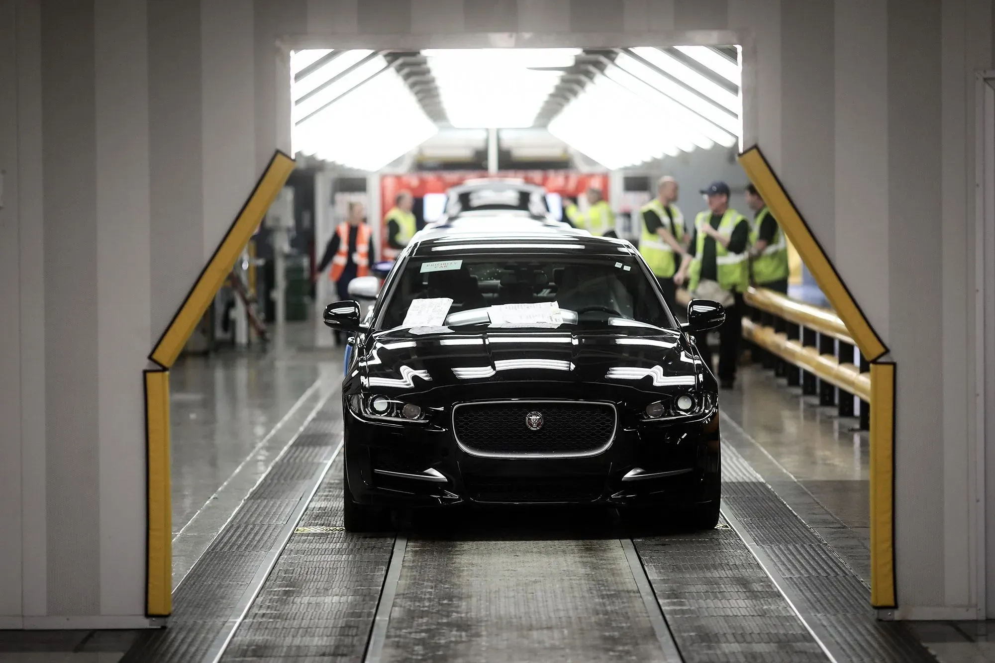 سيارة جاكوار سوداء تسير في خط الإنتاج، مع وجود عمال في الخلفية، تعكس تحديات الشركة في الانتقال نحو السيارات الكهربائية.