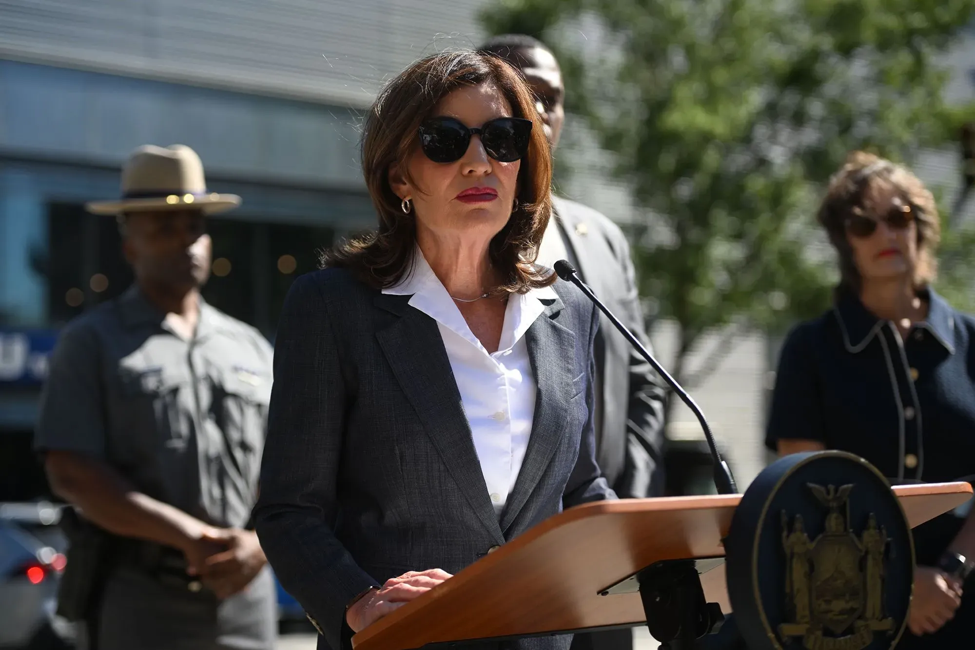 تظهر الصورة حاكمة نيويورك كاثي هوخول تتحدث أمام مجموعة من المسؤولين، في إطار جهود مكافحة سرقة المتاجر وتحسين الأمان.