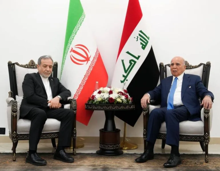 اجتماع بين مسؤول إيراني وآخر عراقي، مع العلمين الإيراني والعراقي خلفهما، في سياق التوترات حول مضيق هرمز.