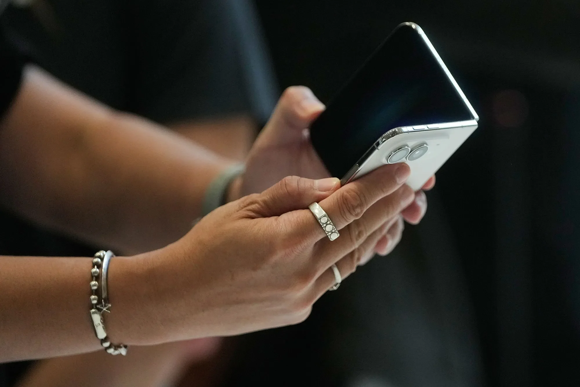 شخص يحمل هاتف iPhone Duo القابل للطي بتصميم يشبه جواز السفر، مع شاشة خارجية سوداء وكاميرتين خلفيتين بارزتين.