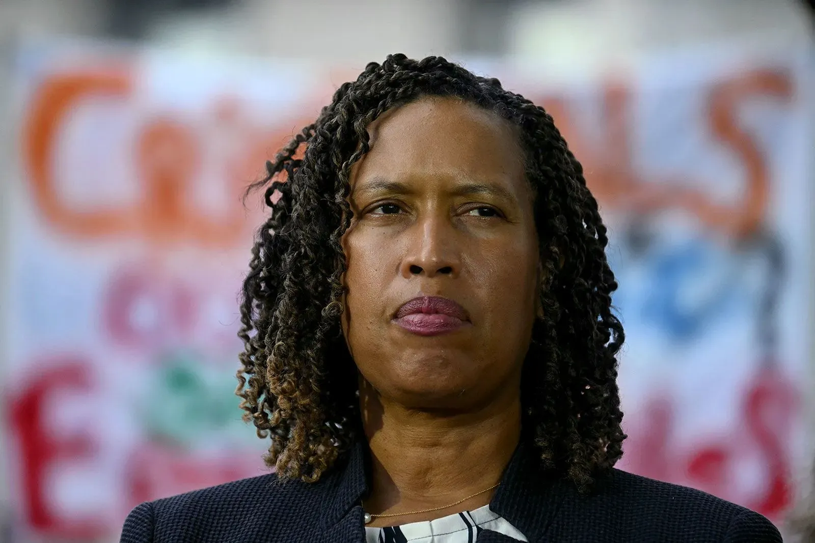 امرأة ذات شعر مجعد ترتدي سترة، تظهر بتعبير جاد في مؤتمر صحفي، مع لافتات خلفها تتعلق بأمن العاصمة واشنطن.