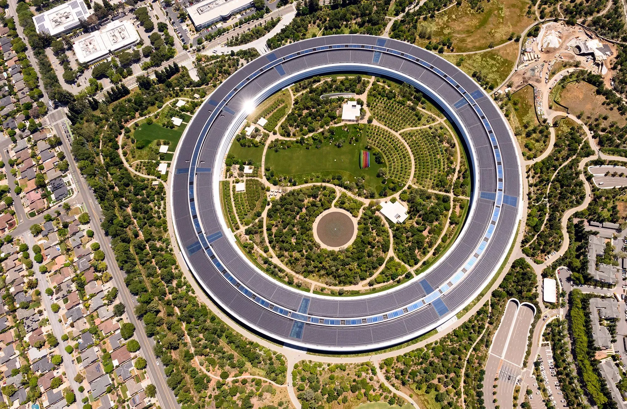 صورة جوية لمقر شركة آبل في كوبرتينو، يظهر التصميم الدائري والحدائق المحيطة، مما يعكس الابتكار والتكنولوجيا المتقدمة.