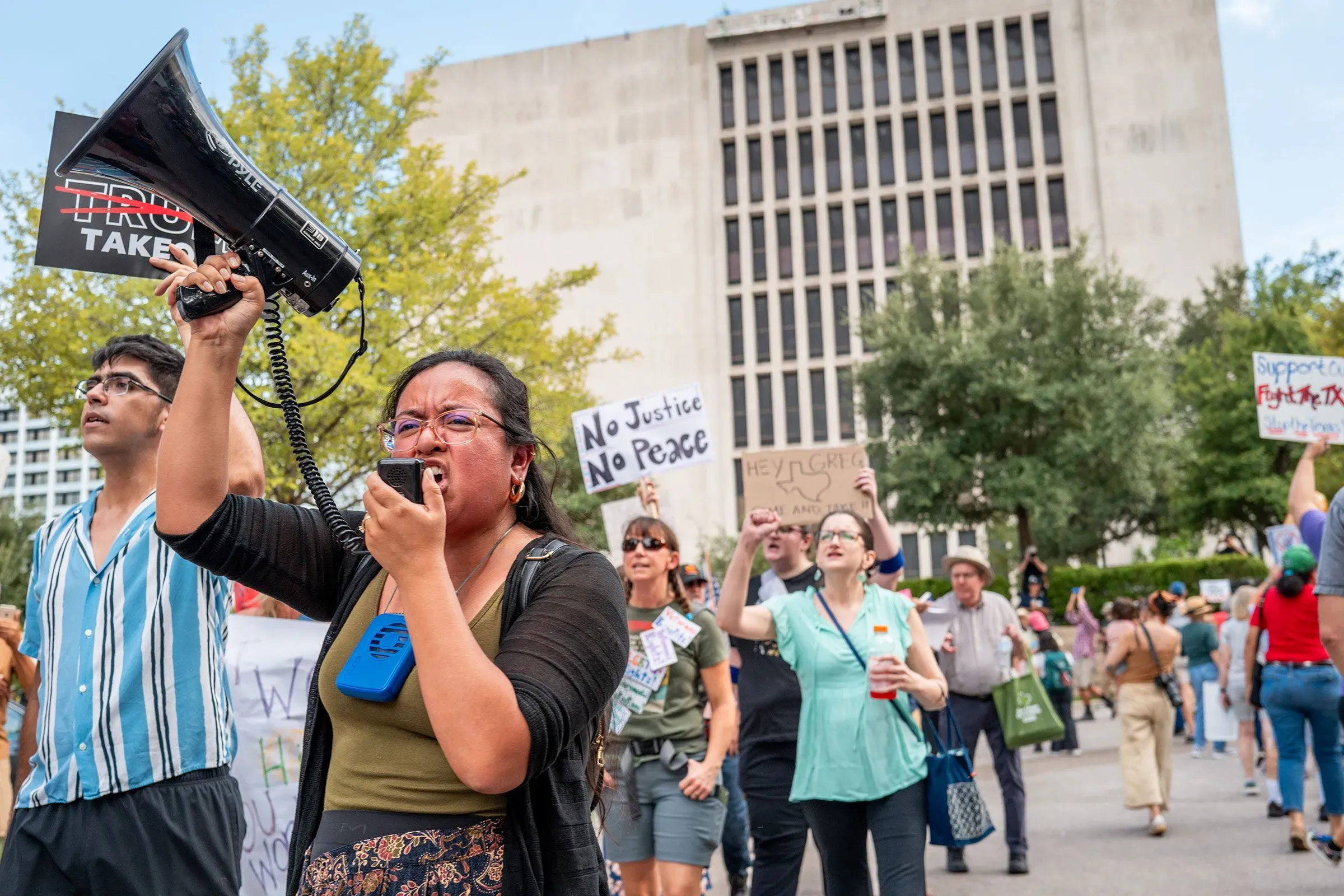 محتجون في تكساس خلال مظاهرة، يحملون لافتات ويستخدمون مكبر صوت للتعبير عن آرائهم حول إعادة تقسيم الدوائر الانتخابية.