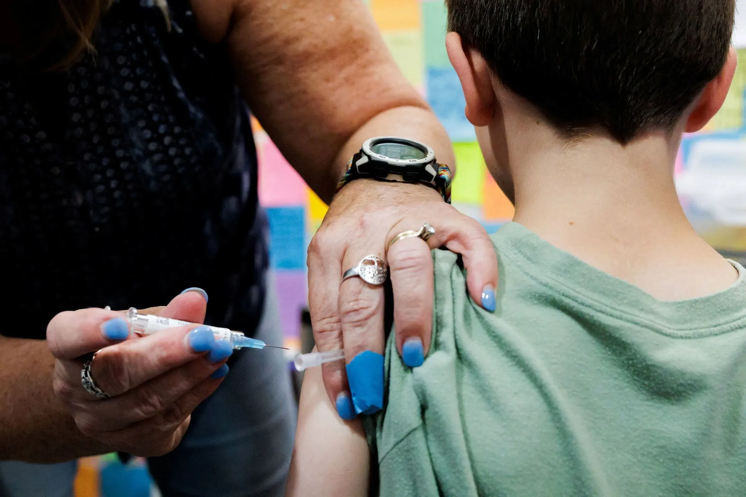 لقاح يُعطى لطفل صغير في مركز صحي، بينما تمسك الملقحة بكتفه. تُظهر الصورة أهمية التطعيم في سياق النقاش حول اللقاحات.