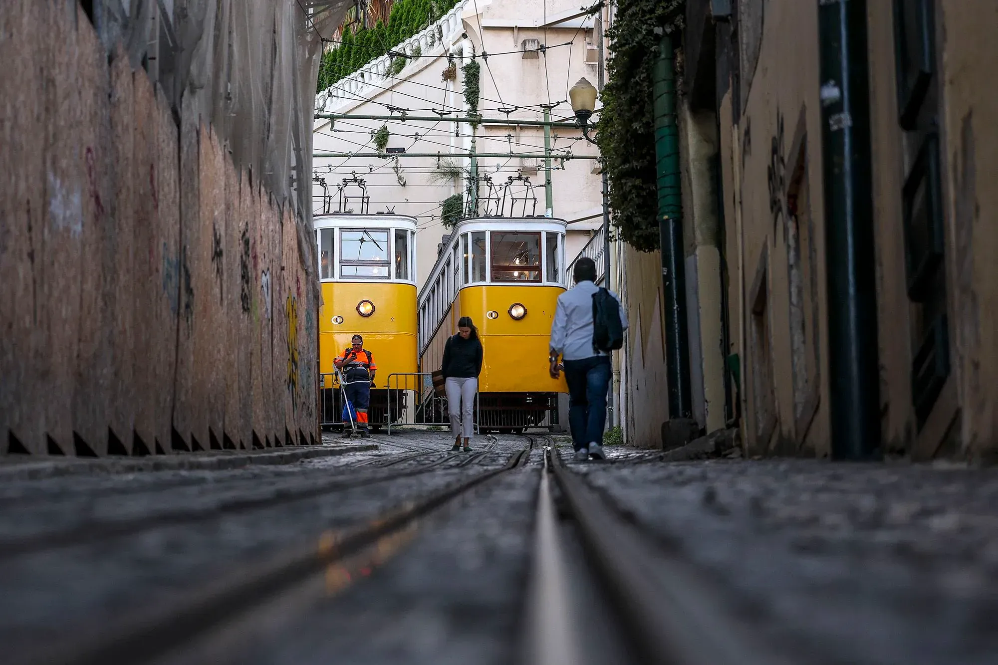 قطار جبلي مائل تاريخي في لشبونة، يظهر عربة صفراء متوقفة في شارع ضيق، مع وجود شخصين بالقرب منها وأثر الحادث واضح.