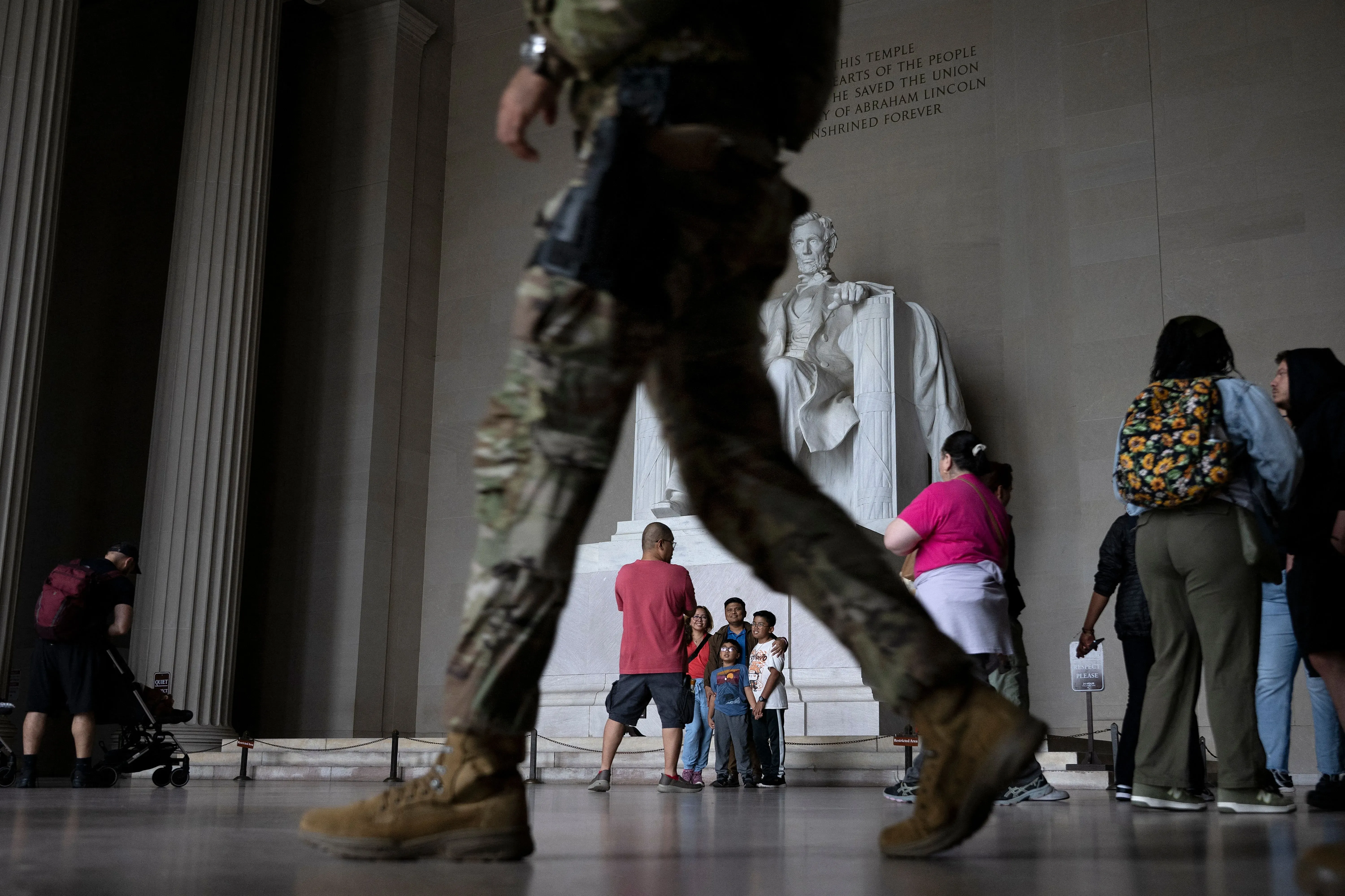 تظهر الصورة جنود يرتدون زيًا عسكريًا بالقرب من نصب لينكولن التذكاري في واشنطن، حيث يتجمع الزوار في الخلفية.