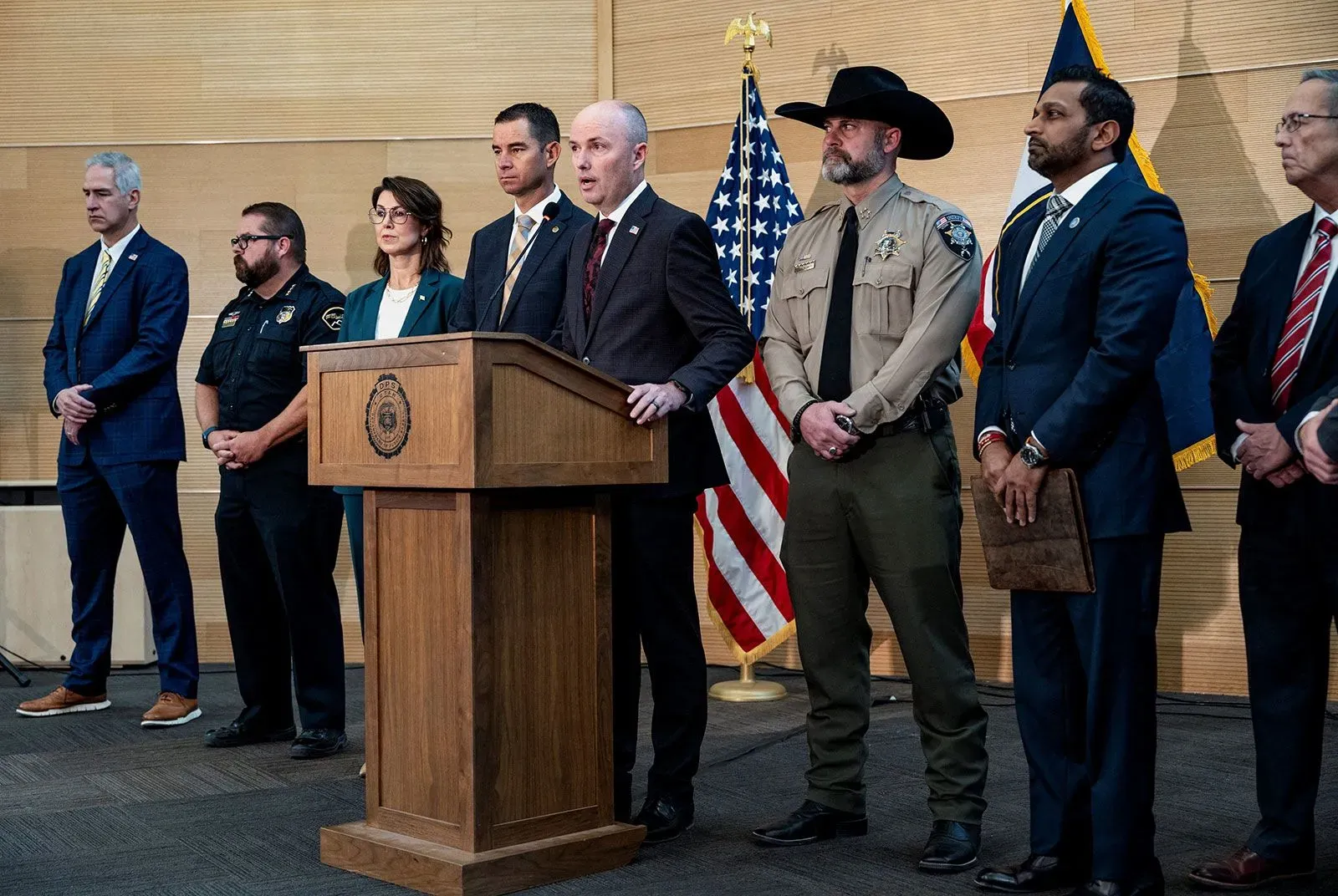 اجتماع للسلطات المحلية مع مسؤولين حكوميين، يتحدثون عن جريمة القتل التي وقعت مؤخرًا، مع العلم الأمريكي في الخلفية.