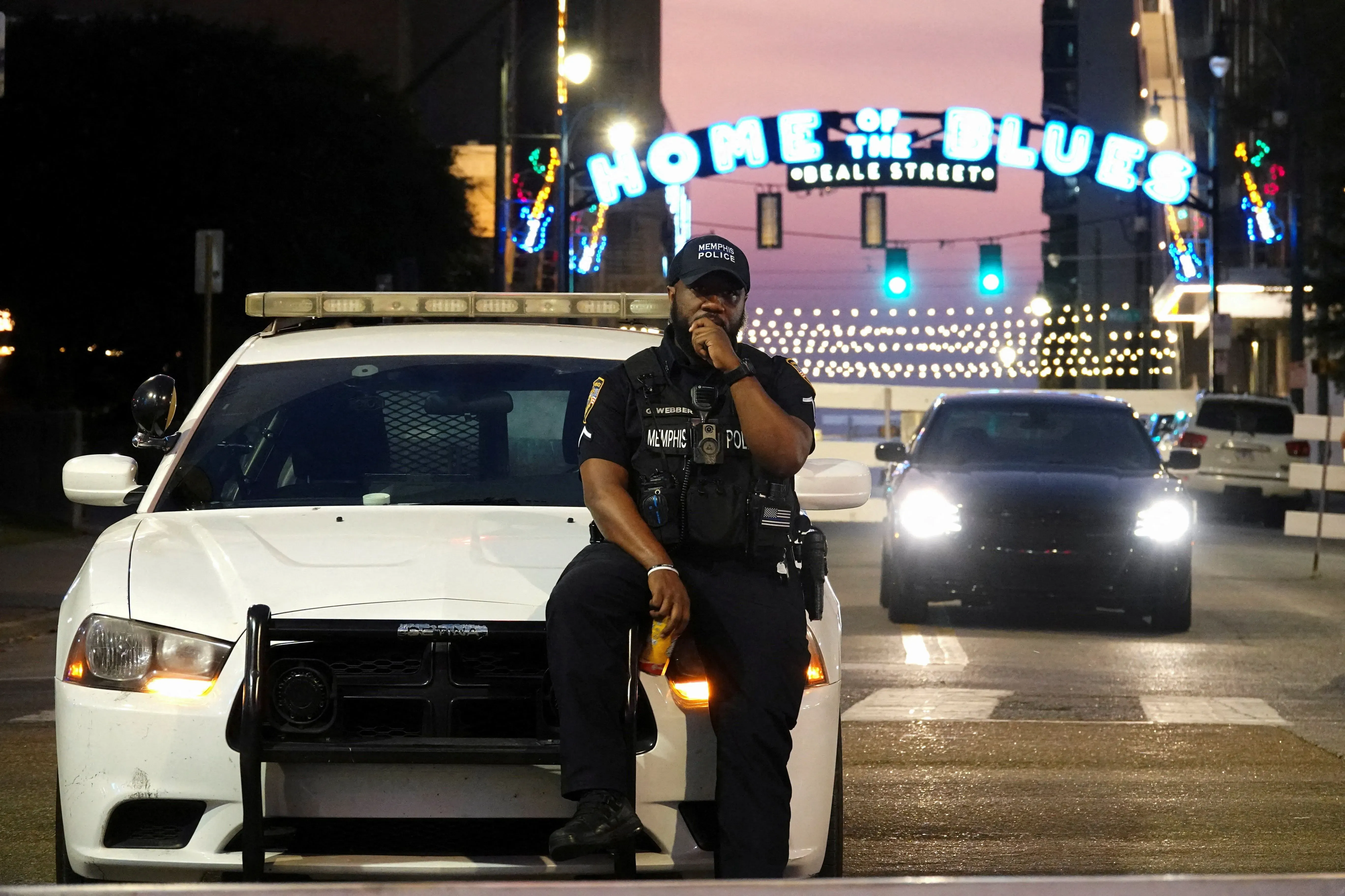 شرطي يجلس على سيارة شرطة في شوارع ممفيس، مع لافتة "Home of the Blues" في الخلفية، وسط جهود الحكومة لمكافحة الجريمة في المدينة.