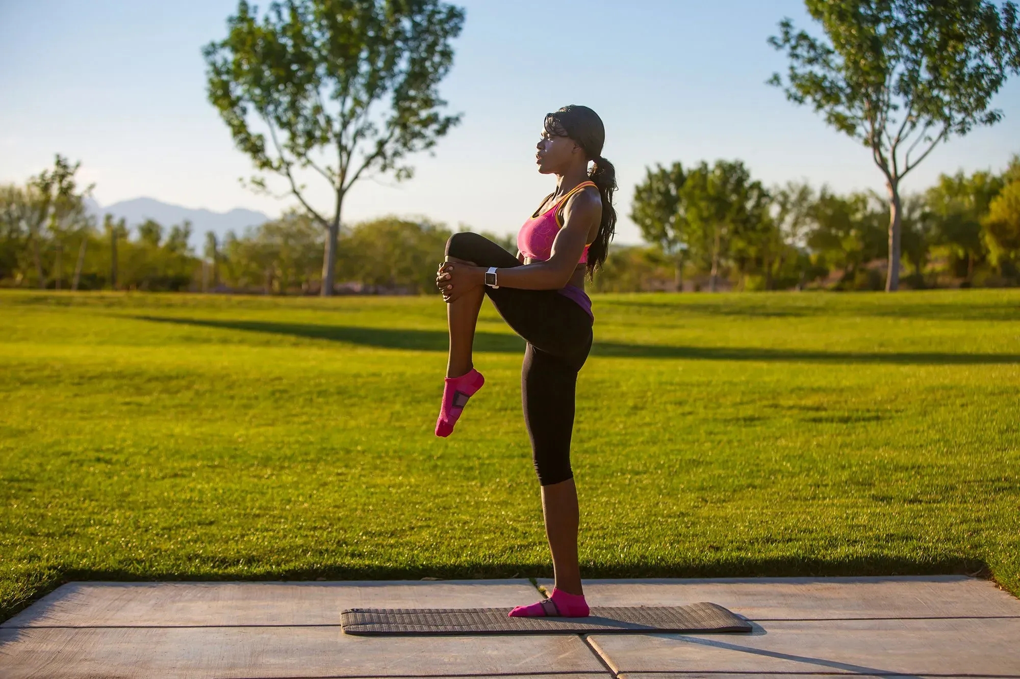 امرأة ترتدي ملابس رياضية تؤدي تمرين رفع الساق في حديقة، مما يعكس أهمية تقوية القدمين لدعم الحركة واللياقة البدنية.
