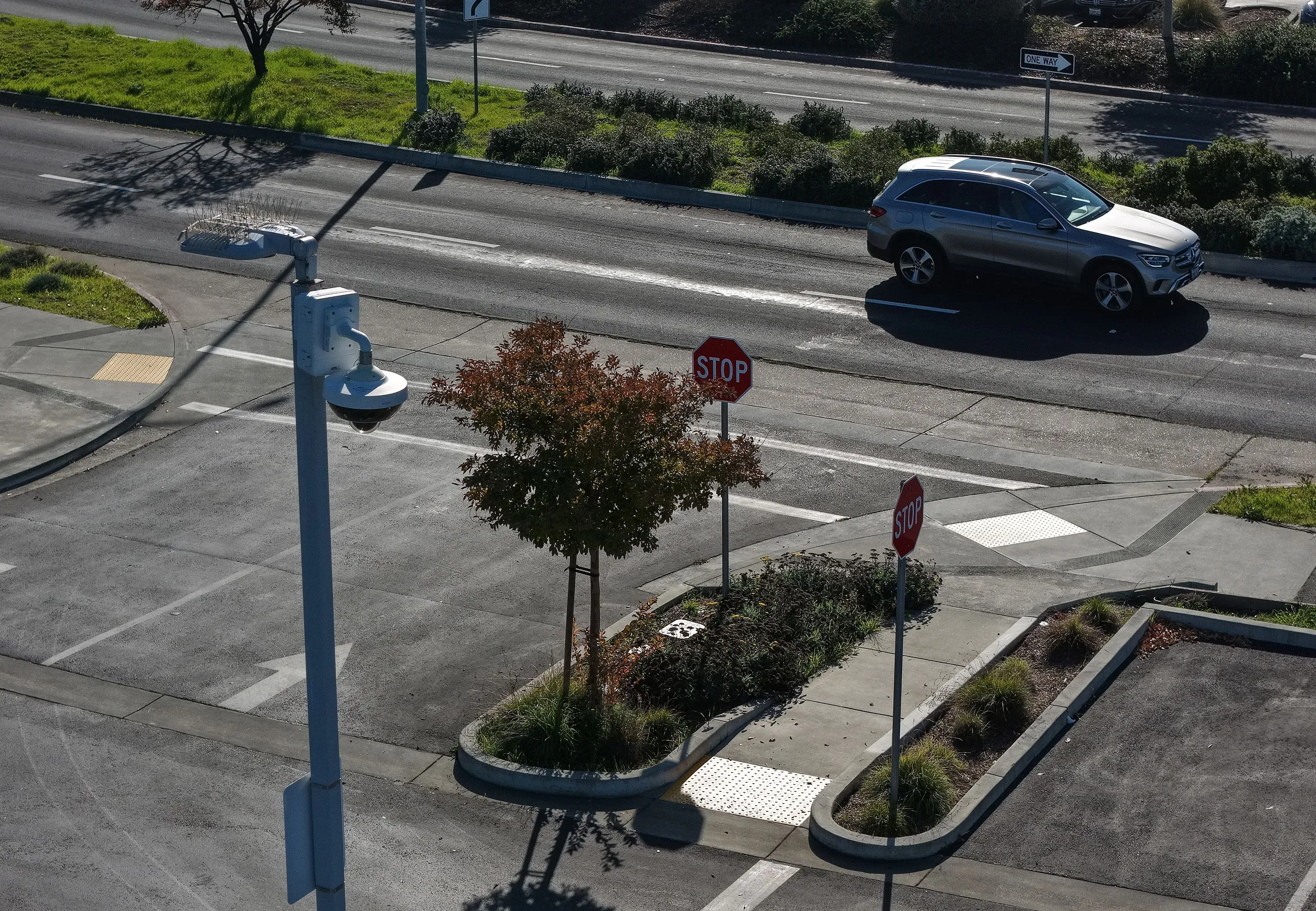 كاميرا مراقبة مثبتة على عمود بجانب تقاطع طرق، مع لافتات توقف وأشجار في الخلفية، تعكس جهود تحسين الأمن في المجتمعات.