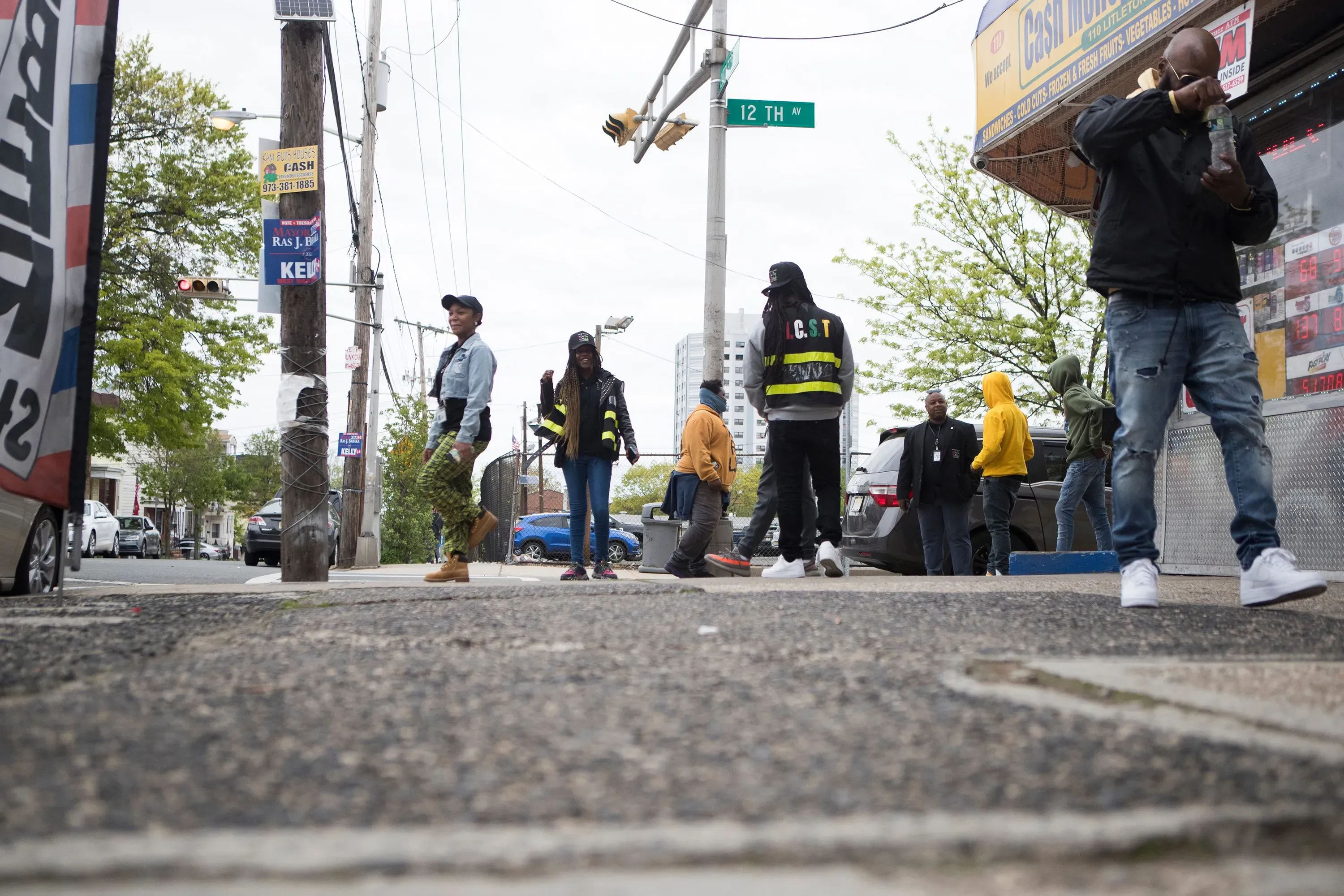 مجموعة من الأشخاص يتجمعون في شارع في نيوارك، نيوجيرسي، مع لافتات ومتاجر محلية، تعكس جهود تقليل العنف في المجتمع.