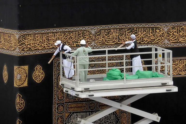 عمال يقومون بتغيير الكسوة السوداء للكعبة المشرّفة، مع التركيز على التفاصيل المطرّزة بالذهب، خلال موسم الحج في مكة المكرّمة.