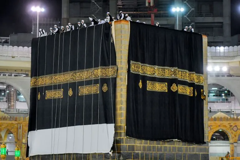 تظهر الكعبة المشرّفة مغطاة بالكسوة السوداء المطرّزة بخيوط الذهب، مع الحجاج يتواجدون حولها في أجواء الحج.