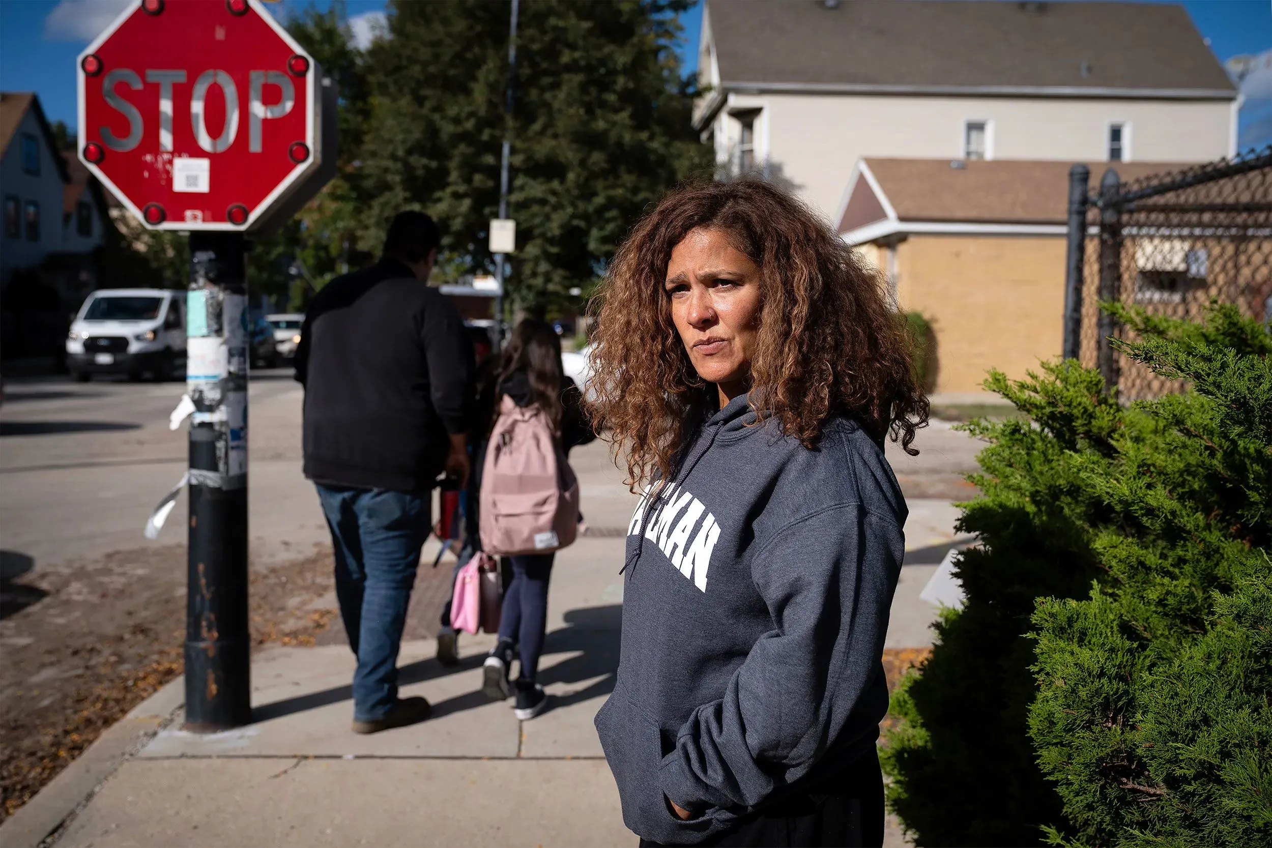 امرأة ترتدي سترة رمادية وتقف بجوار علامة توقف، بينما يرافقها أطفال في حي ويست ريدج بشيكاغو، في سياق مخاوف من مداهمات الهجرة.