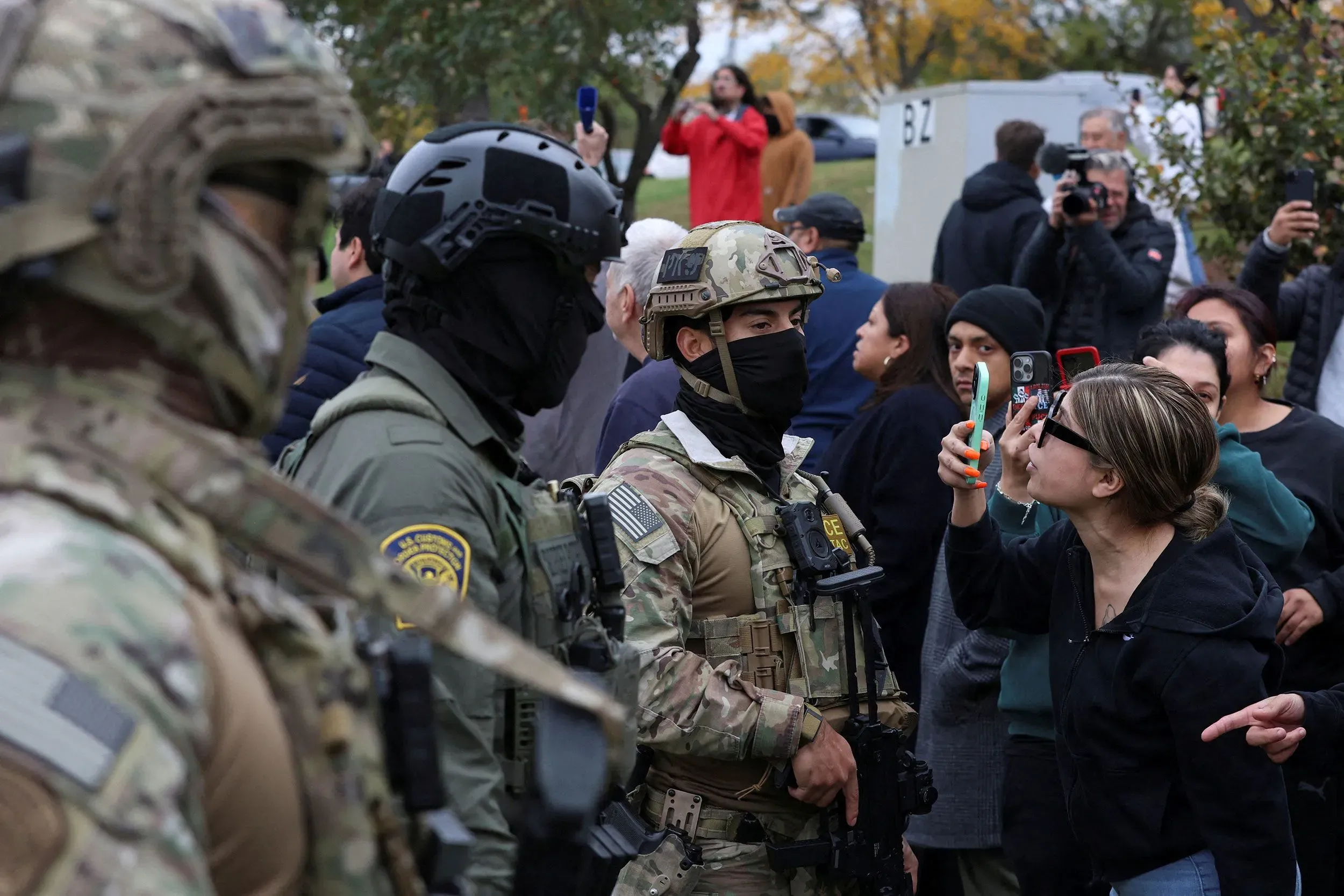 محتجون يتفاعلون مع عملاء إنفاذ الهجرة في شيكاغو، مع وجود أفراد يرتدون زياً عسكرياً، بينما يتجمع الناس حولهم.