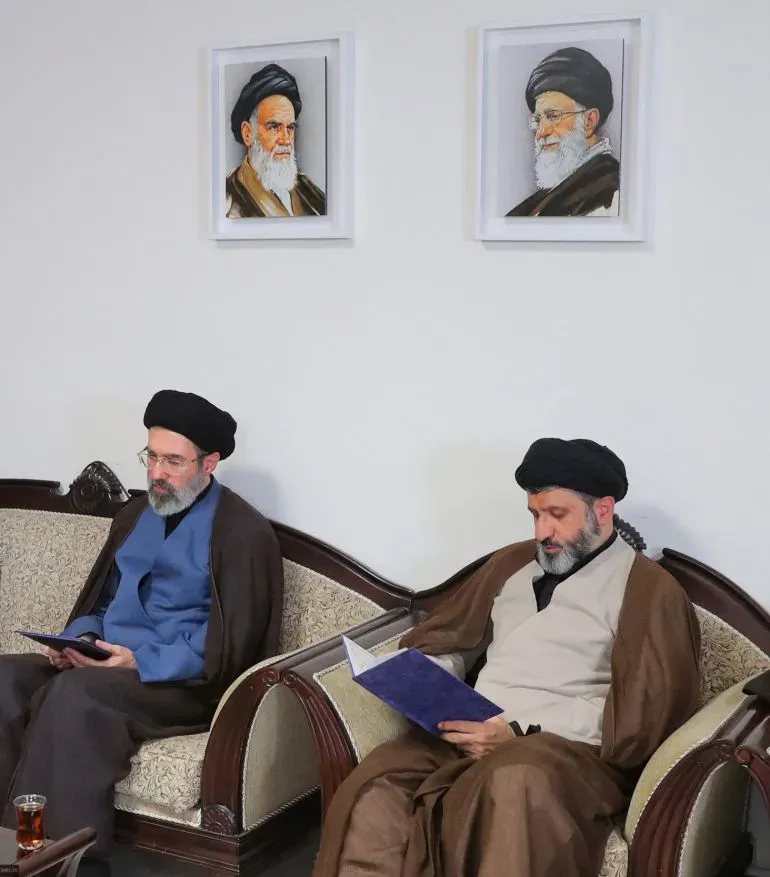 اجتماع لعدد من رجال الدين الإيرانيين، يجلسون على الأرائك في غرفة بسيطة، بينما يقرأون من كتبهم، مع صور للمرشدين السابقين على الجدران.